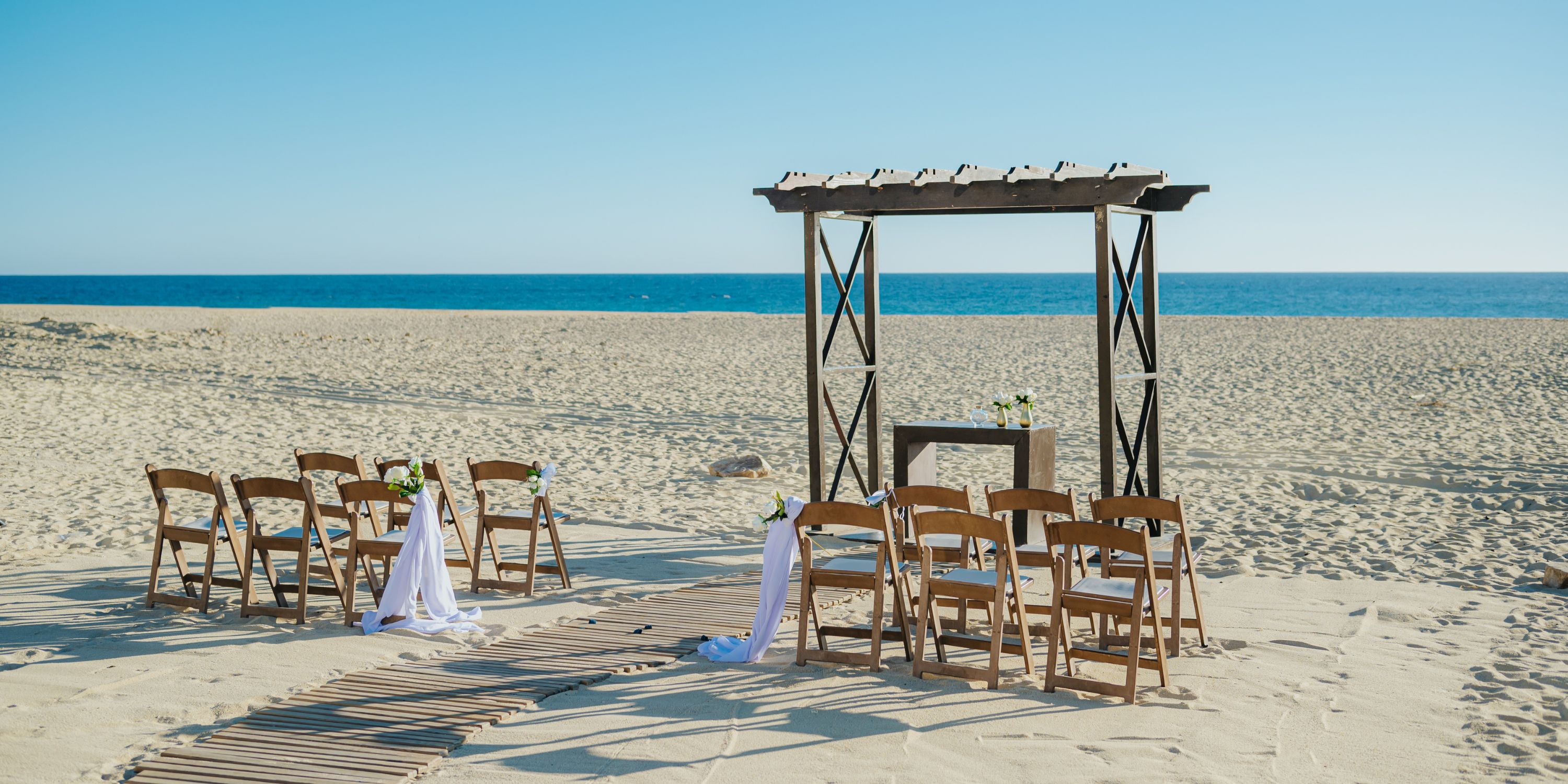 Hard Rock Los Cabos presents a destination wedding setup with chairs and an arch on the sandy beach.