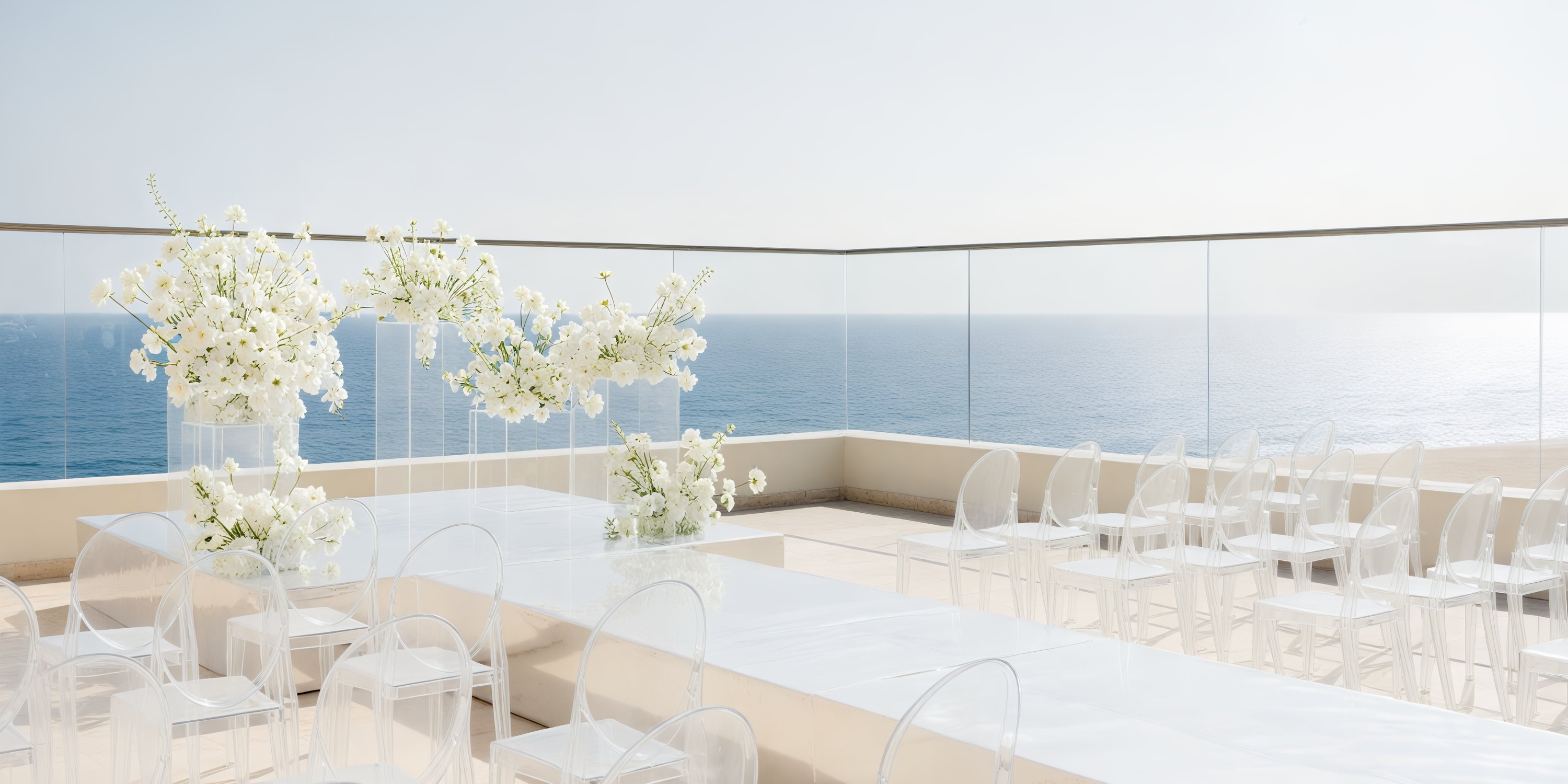 Experience the breathtaking destination wedding setup on the rooftop at Hard Rock Los Cabos, featuring elegant white flowers, clear chairs, and a stunning ocean view.