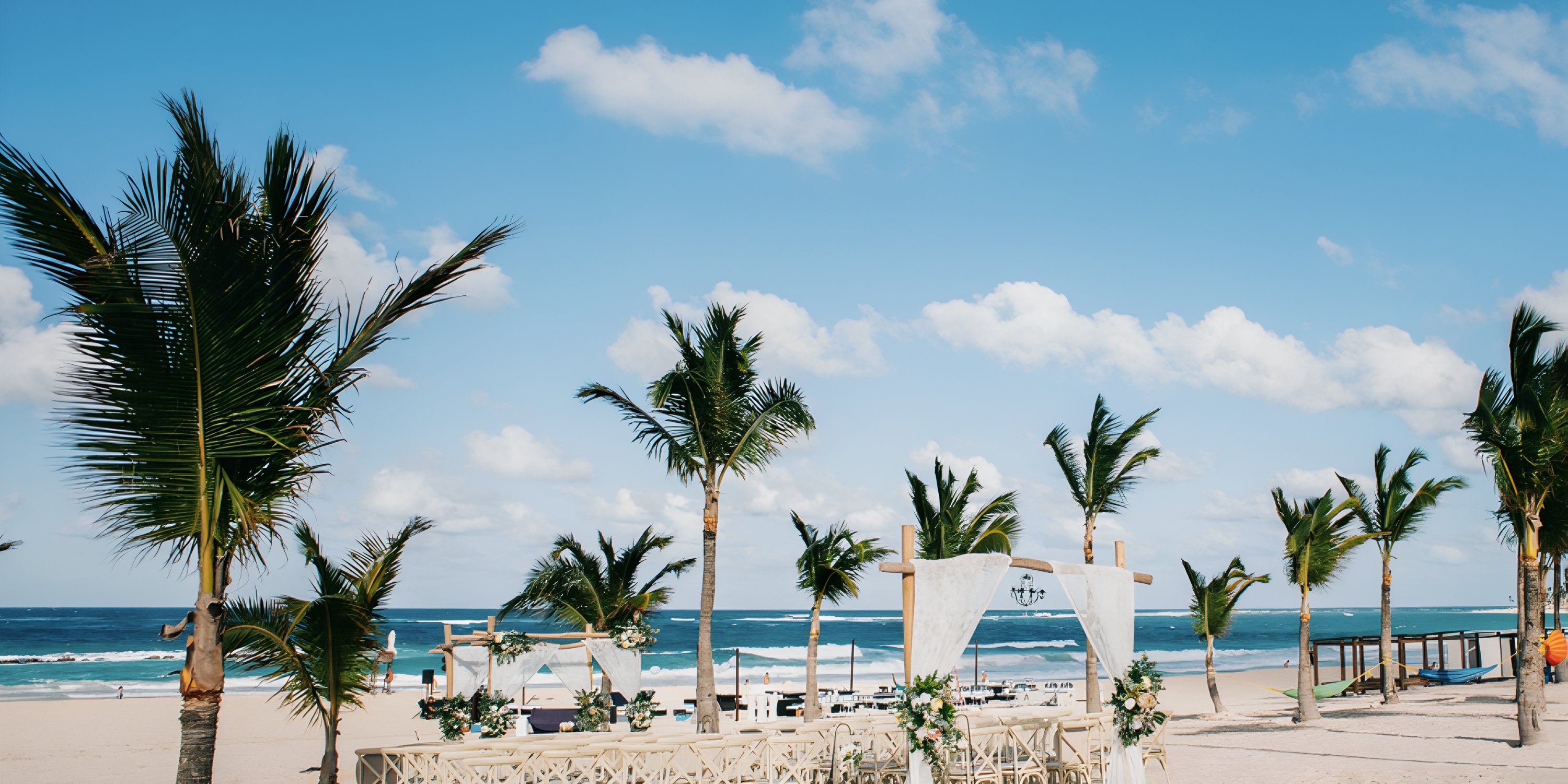 Destination wedding setup at Hard Rock Punta Cana with white d&eacute;cor, palm trees, and ocean backdrop.