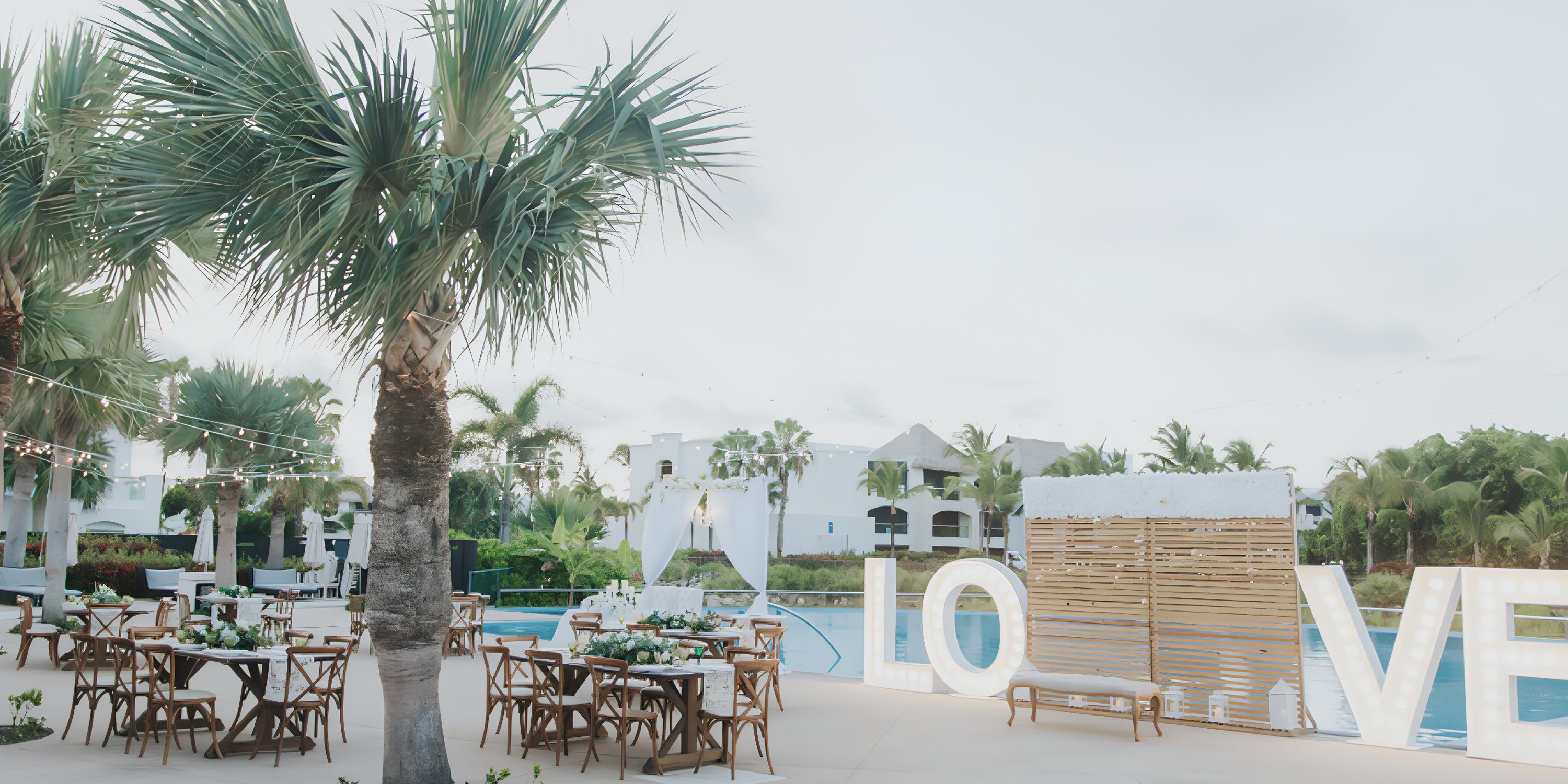 Destination wedding poolside setup at Hard Rock Punta Cana with tables, palms, and "LOVE" letters.