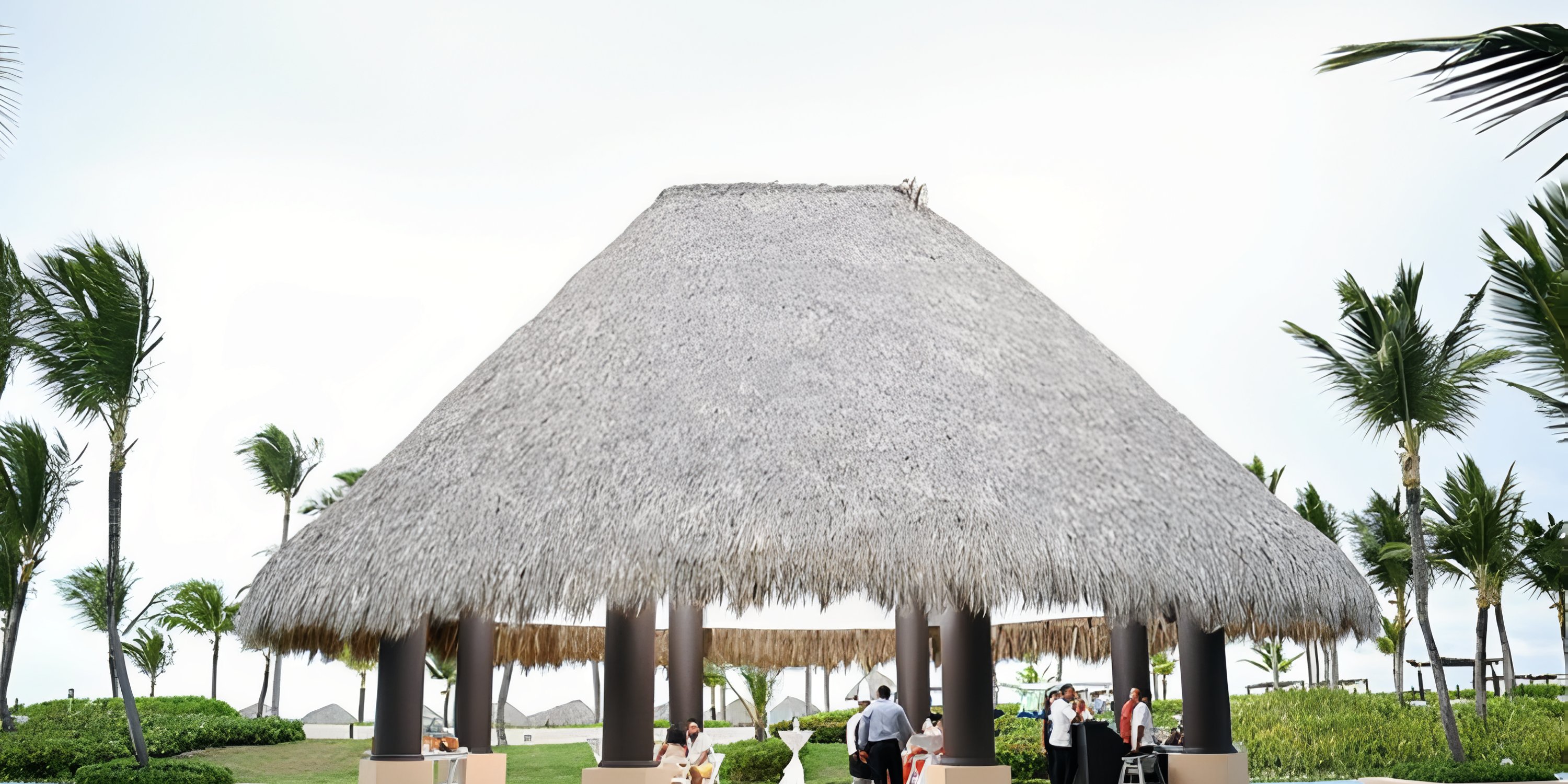 Guests mingle beneath a thatched-roof pavilion at Hard Rock Punta Cana, a scenic destination wedding venue.