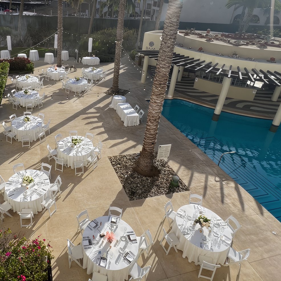 Outdoor poolside area arranged with round tables and white chairs, perfect for a destination wedding event.