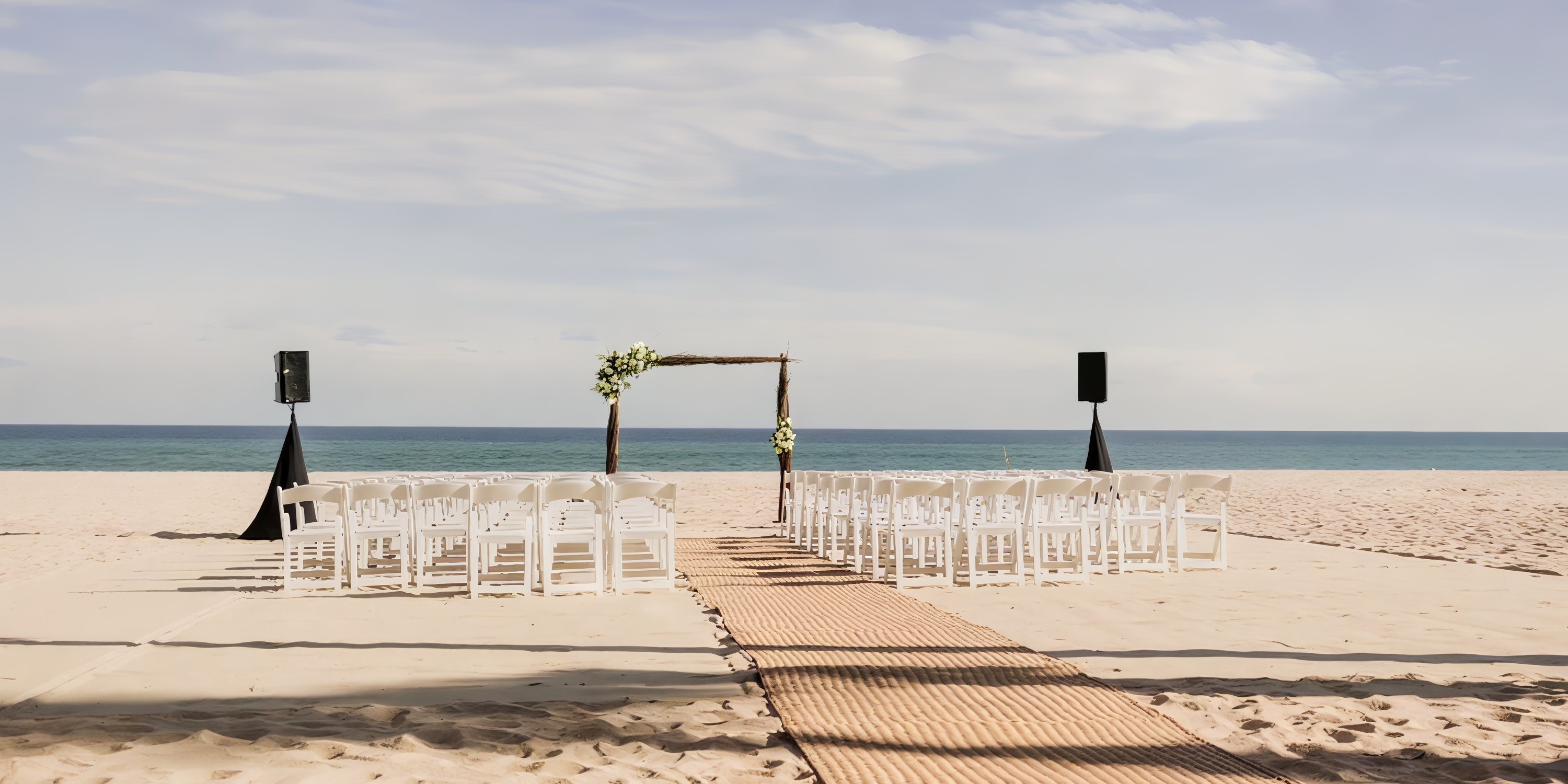 White chairs face a wooden arch on the sand at Hyatt Ziva Los Cabos, arranged for a destination wedding.
