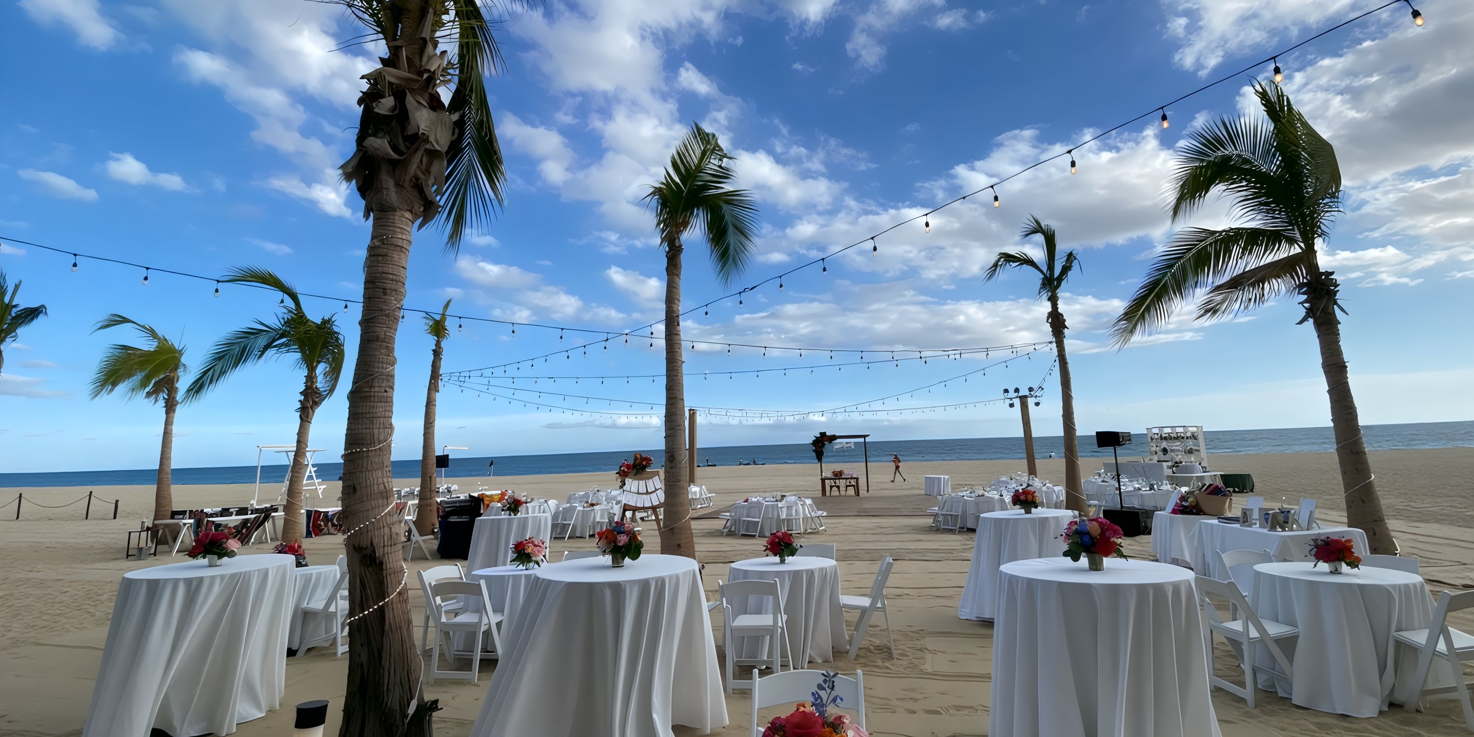 Hyatt Ziva Los Cabos wedding setup on the beach with round tables, white linens, palms, and string lights.