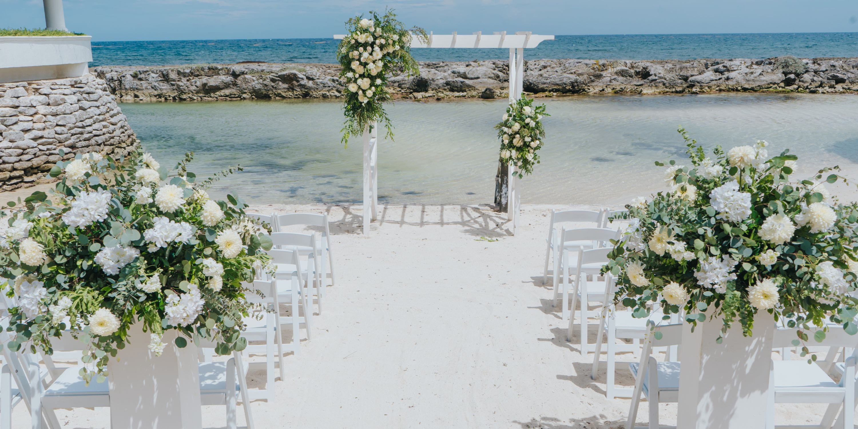 White chairs and florals arranged for a destination wedding at Hard Rock Riviera Maya beach resort.
