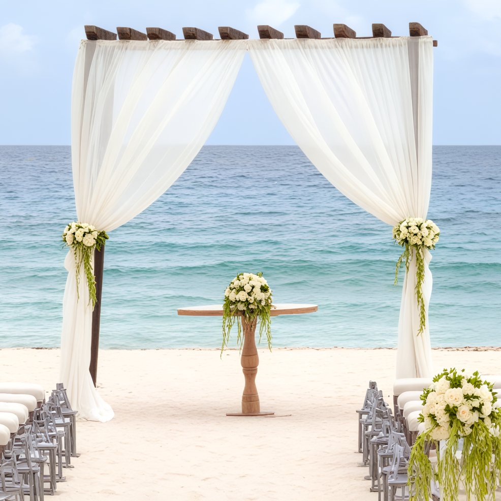 Destination wedding altar on the beach, adorned with white drapes, flowers, and overlooking the ocean.