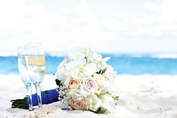 Royalton Bavaro: A picturesque wedding setting featuring a bouquet and champagne glasses on the sandy beach with the sparkling ocean as your destination wedding backdrop.
