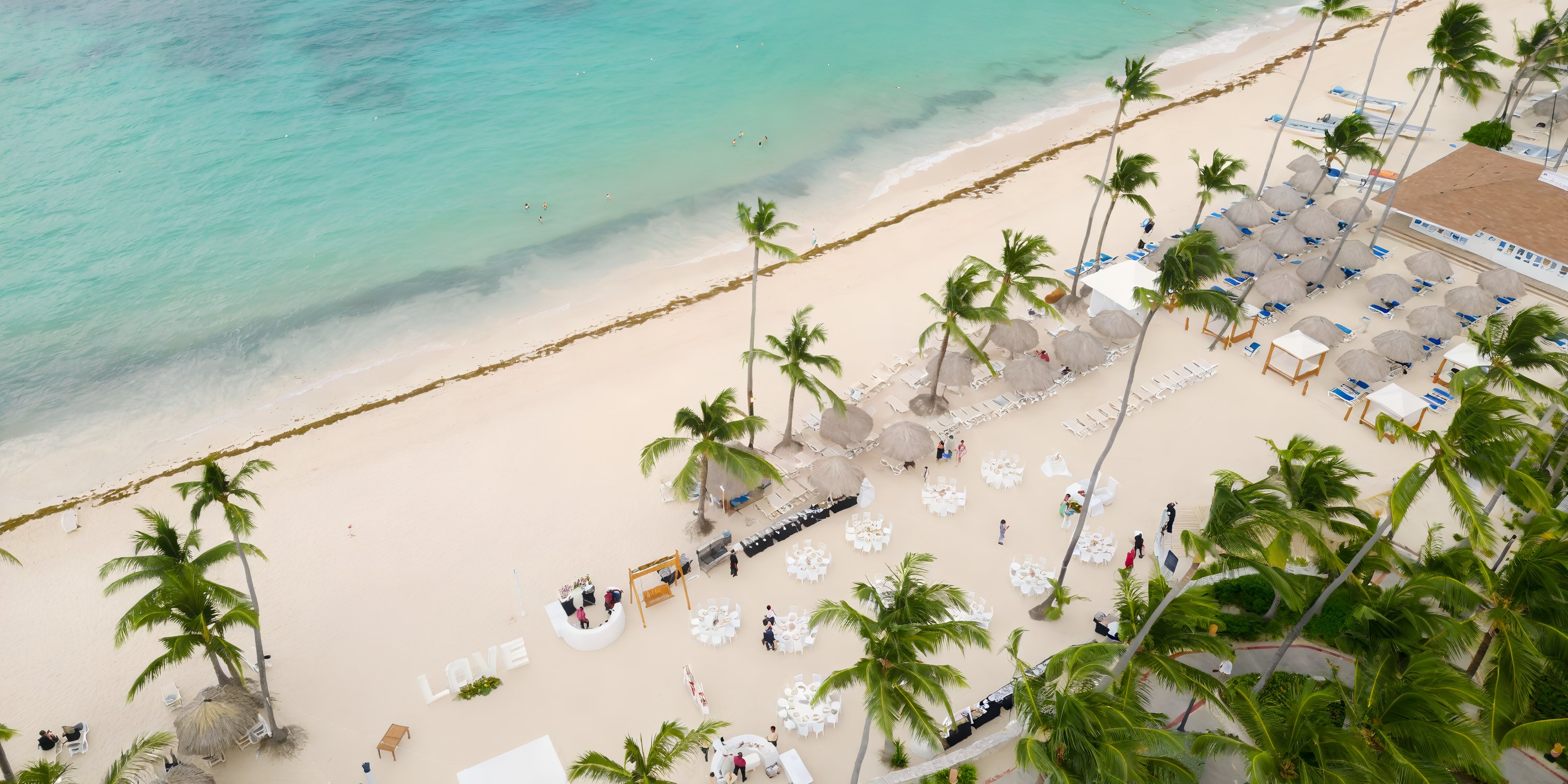 Aerial view of Majestic Elegance Punta Cana, palm trees, white sand, and a destination wedding setup.
