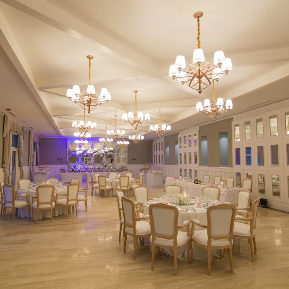 Elegant banquet hall with chandeliers, round tables, and white chairs set up for a destination wedding.