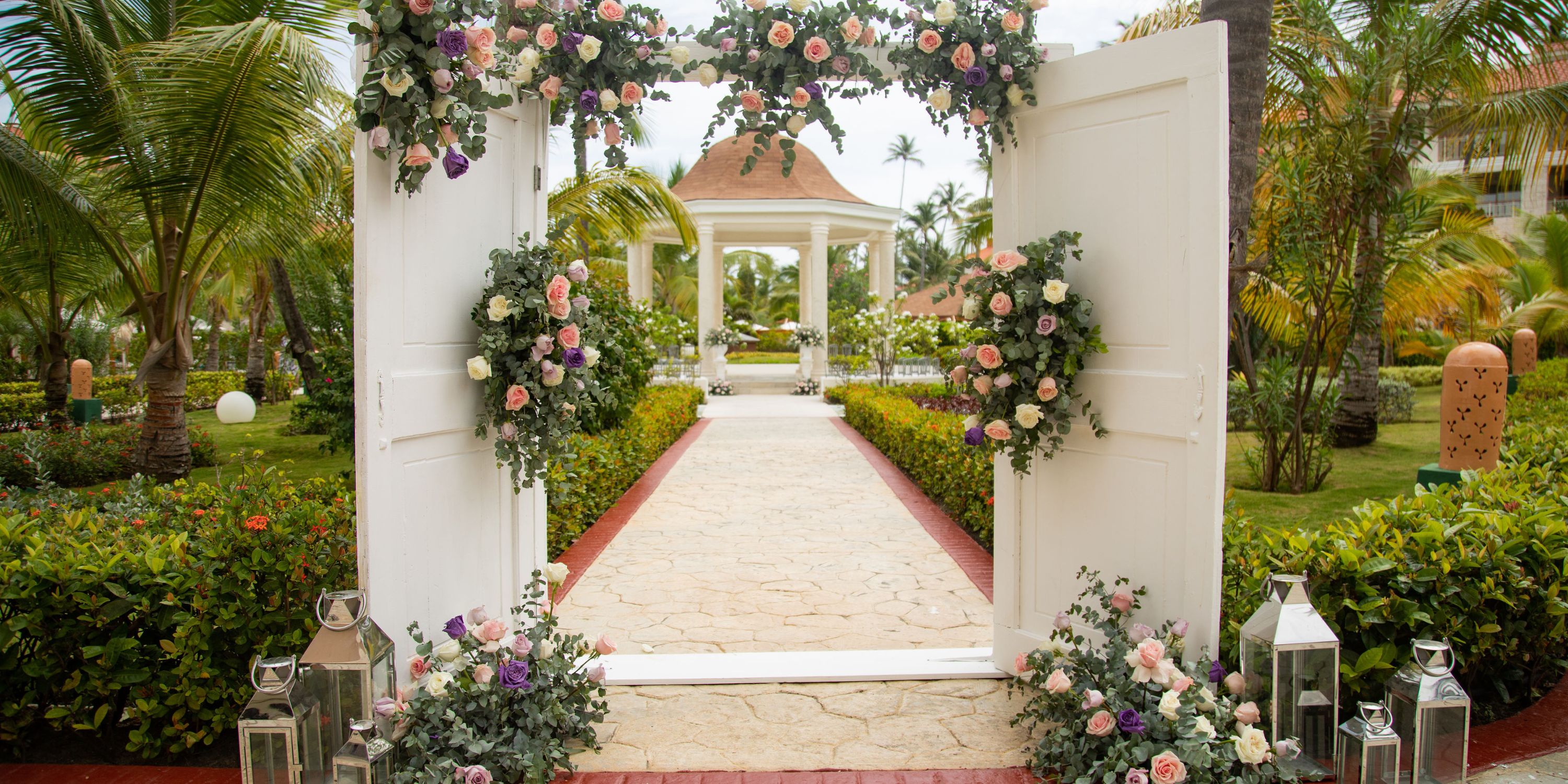 Flower-adorned white doors open to a garden path, perfect for a destination wedding at Majestic Mirage.