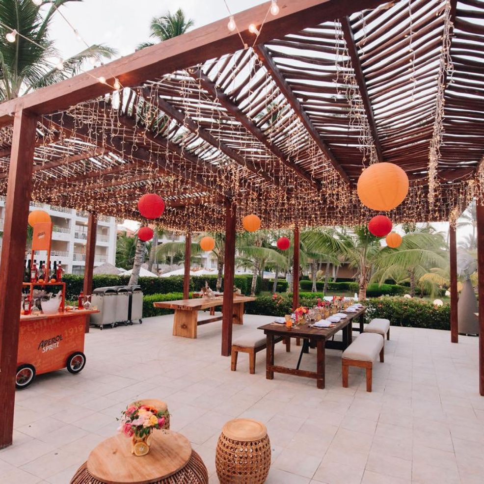 Outdoor patio with wooden pergola, string lights, lanterns, and set dining tables for a destination wedding.