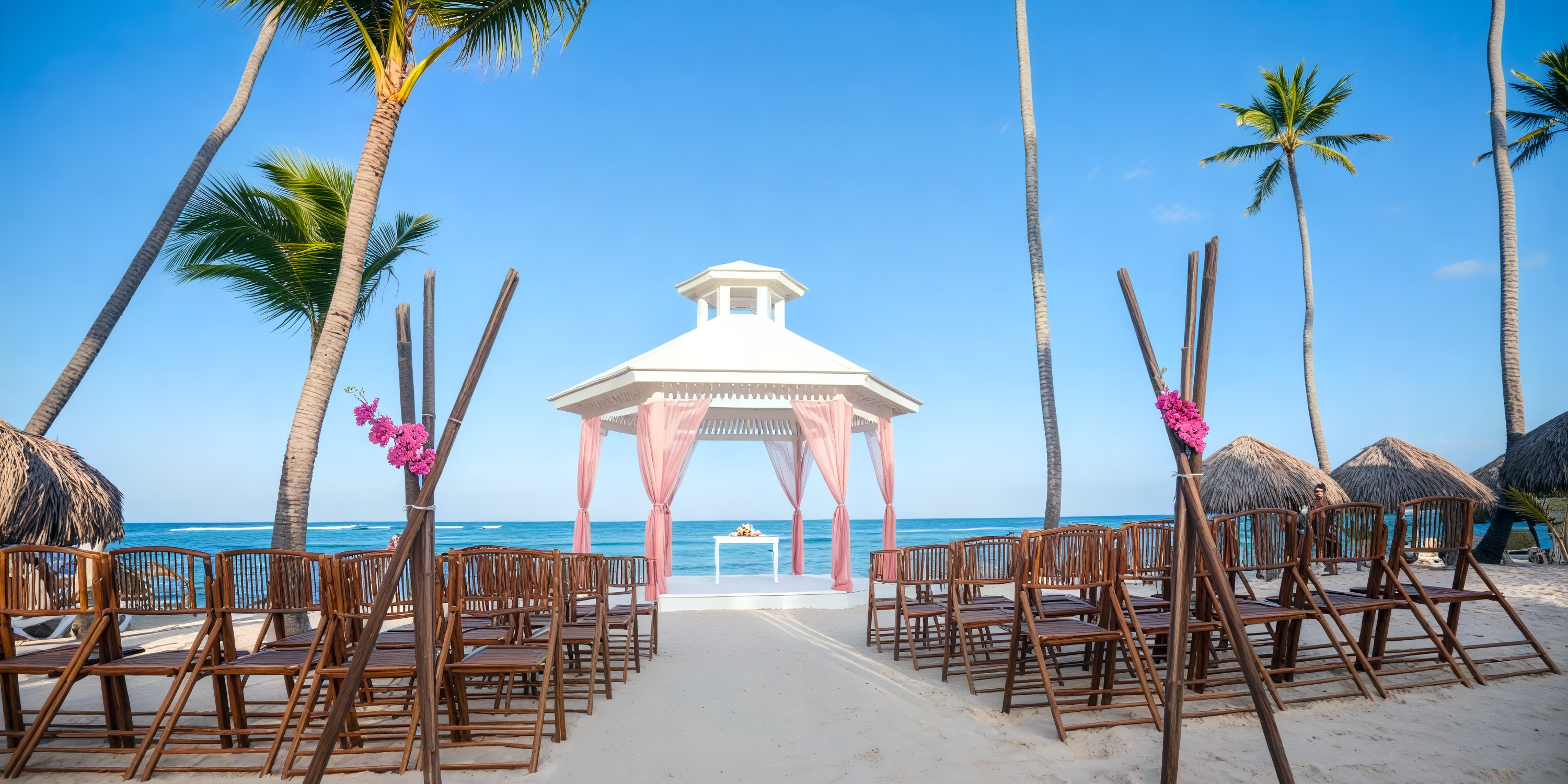 Destination wedding at Majestic Colonial with rows of chairs facing a white gazebo under tall palm trees.