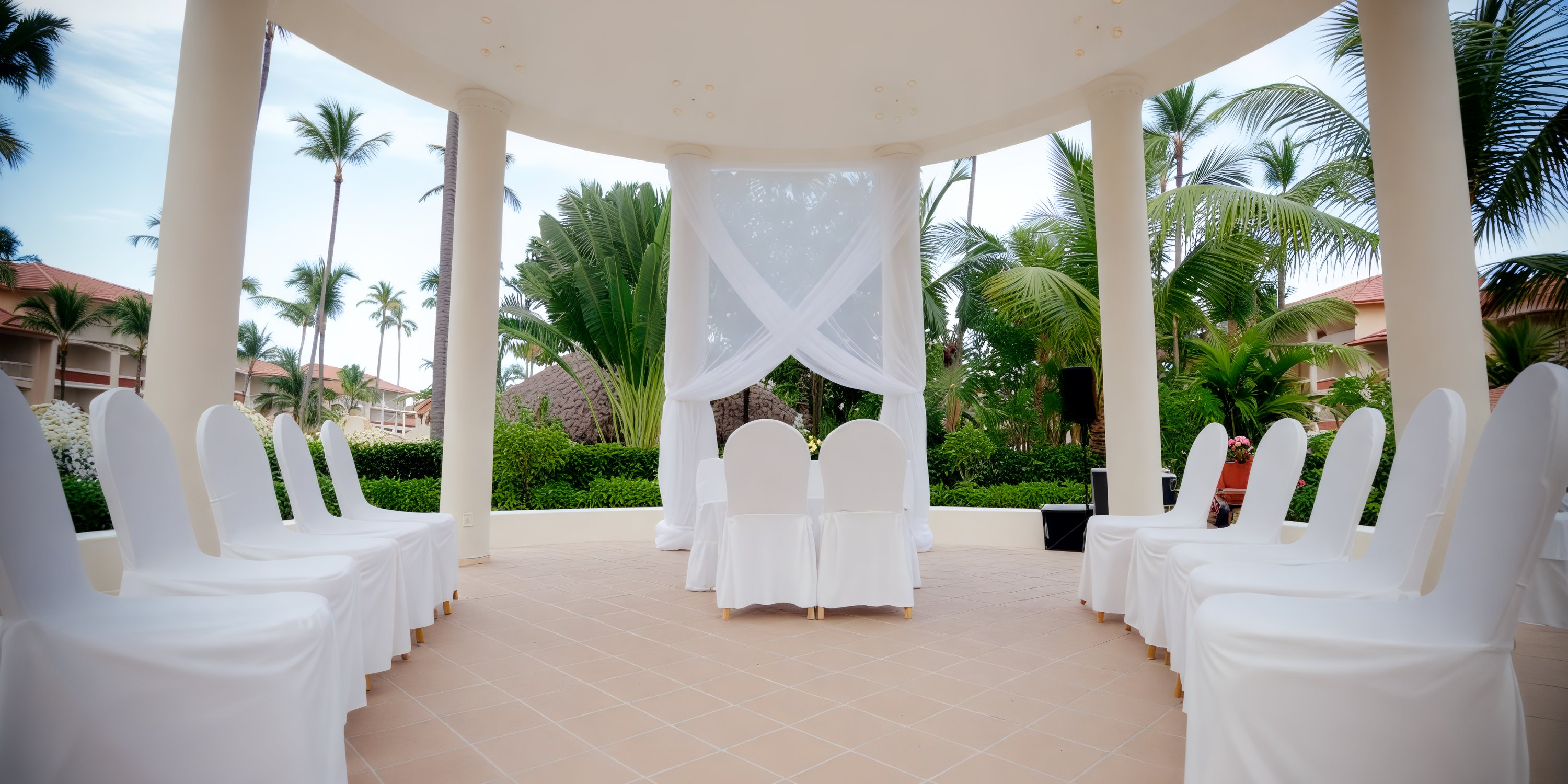 Elegant destination wedding setup featuring white chairs and a pavilion canopy draped for the ceremony.