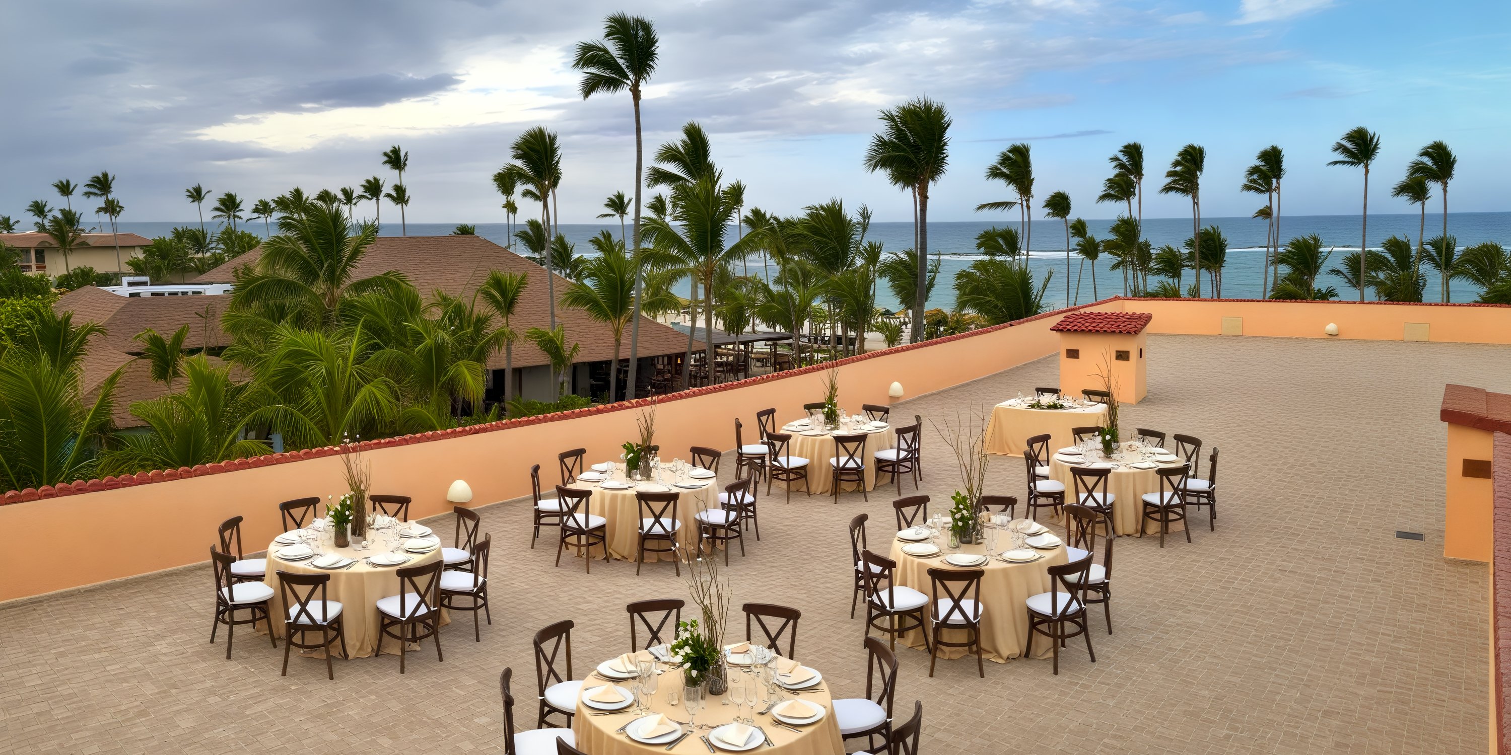 A destination wedding at Majestic Colonial features round tables arranged on an oceanfront terrace.