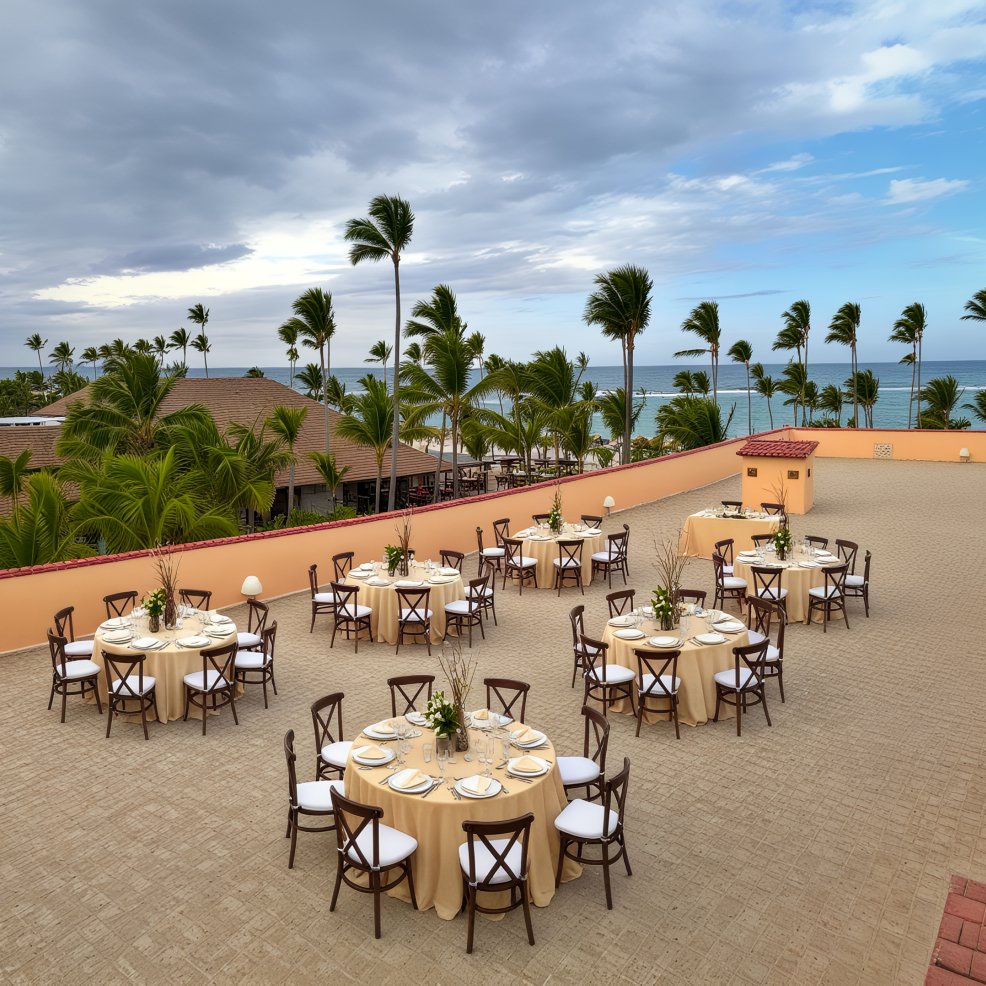 Round tables with beige tablecloths arranged for a destination wedding on an oceanfront terrace.