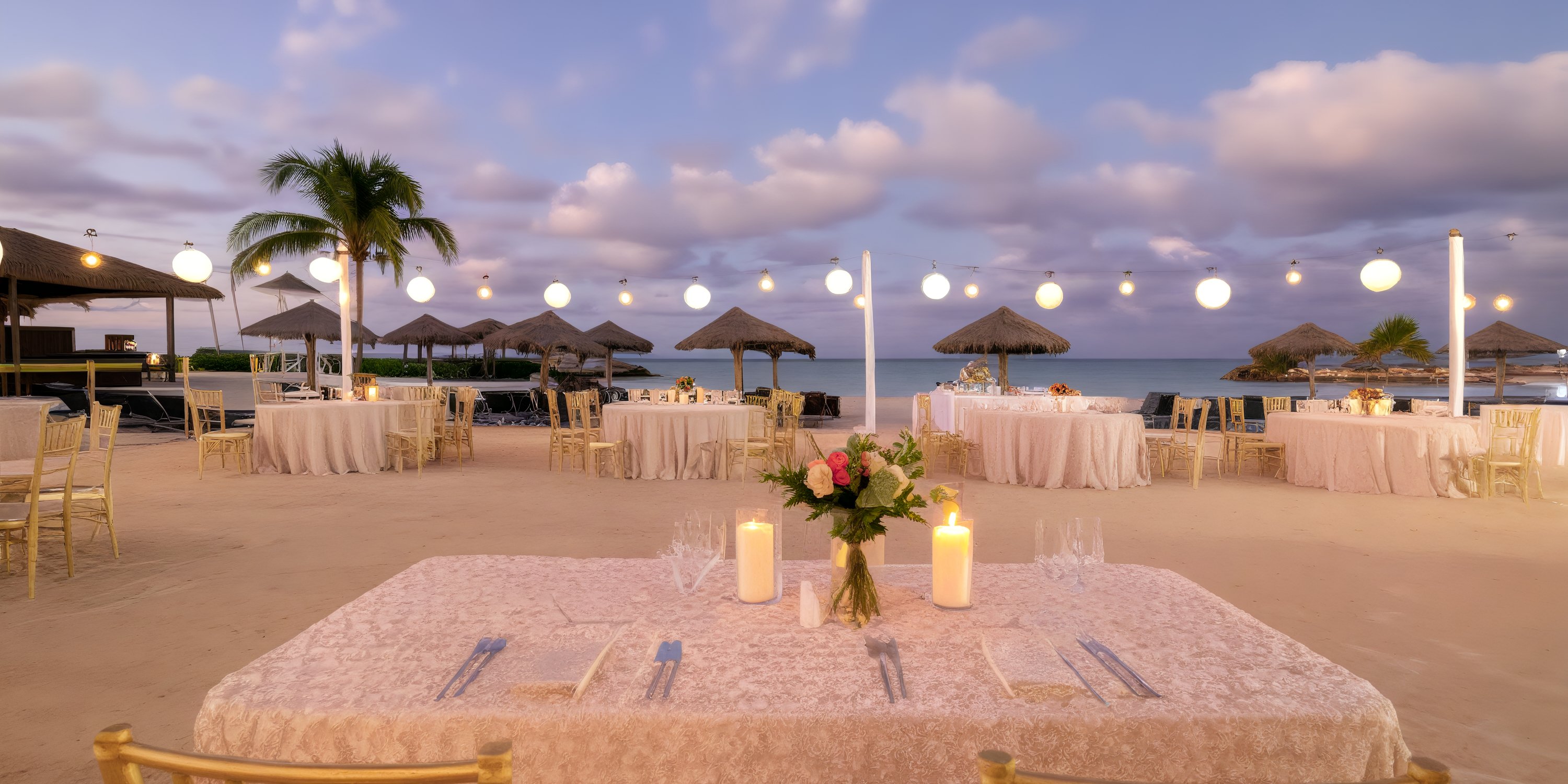 Tables set at sunset with candles and hanging lights, ready for a destination wedding at Royalton Blue Waters.