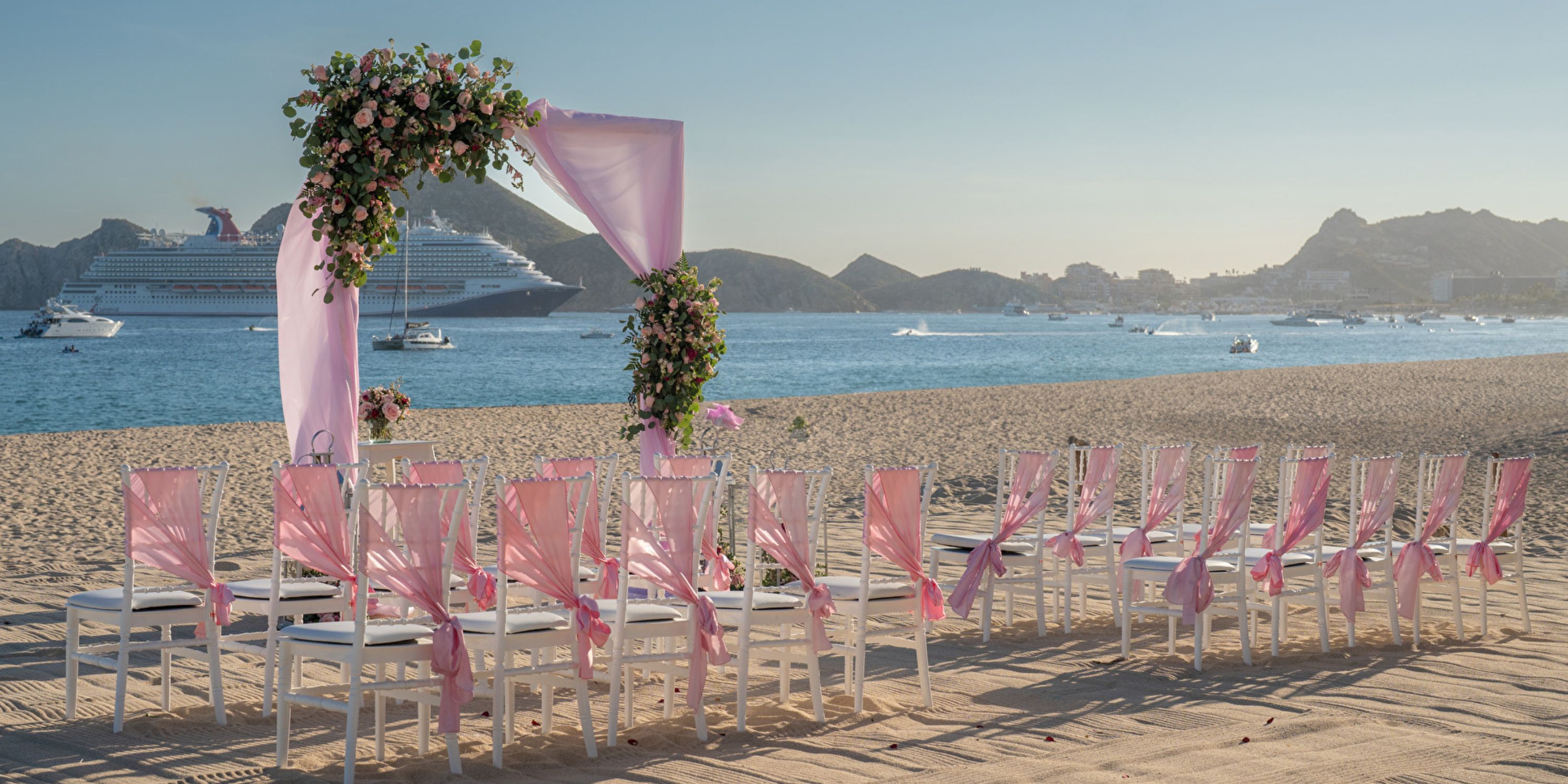 Chairs with pink decorations and a floral arch arranged for a destination wedding at Hotel Riu Santa Fe.