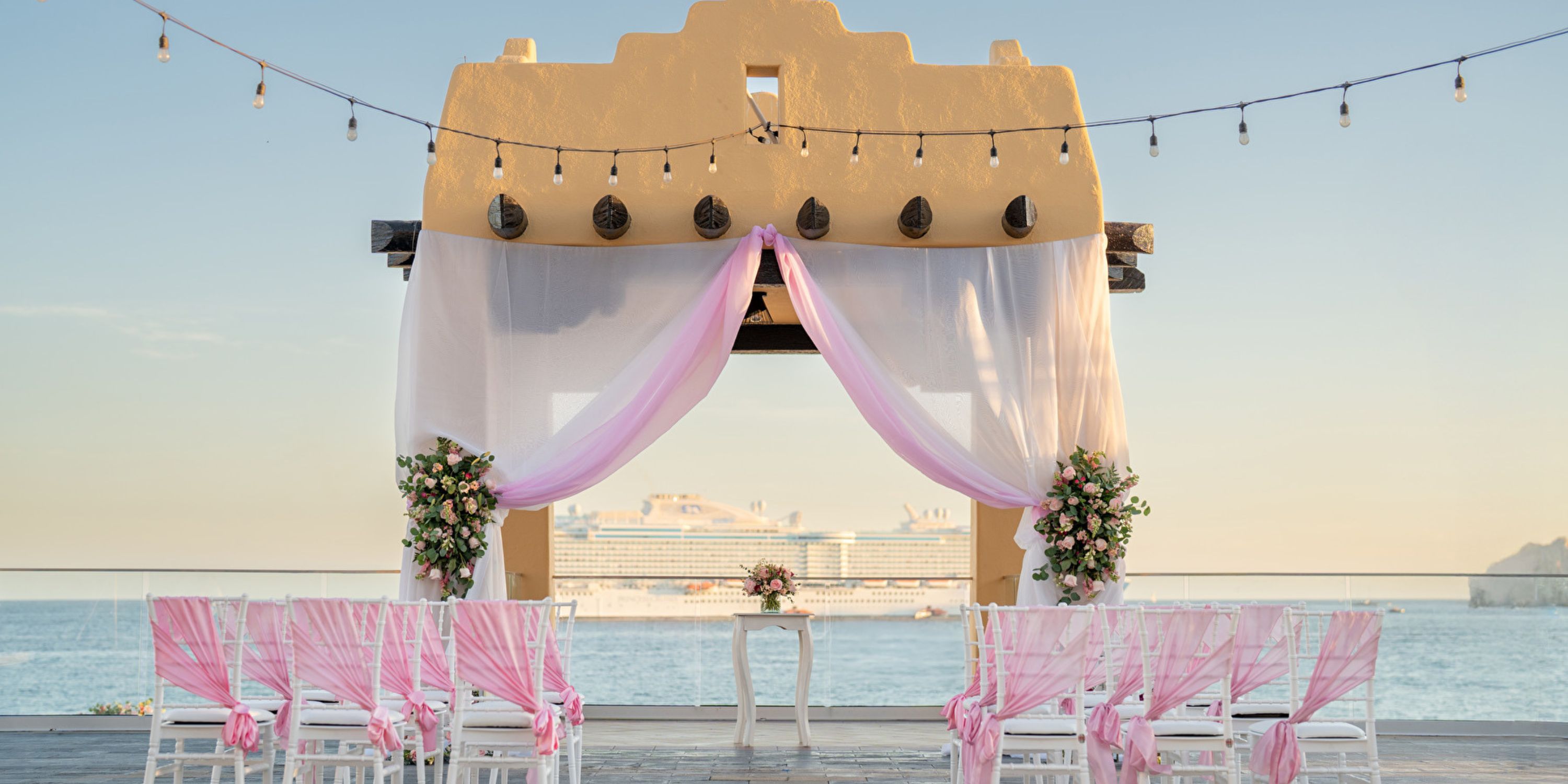Destination wedding at Hotel Riu Santa Fe with pink and white decor, sea views, and a cruise ship nearby.