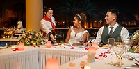 Bride and groom smile during their destination wedding dinner as food is served at Hotel Riu Santa Fe.