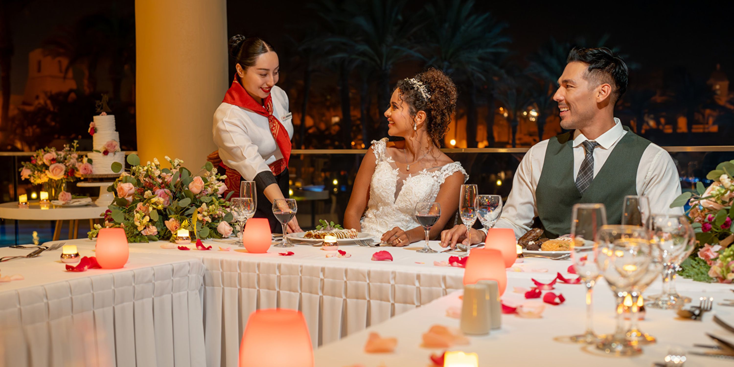 Bride and groom smile during their destination wedding dinner as food is served at Hotel Riu Santa Fe.