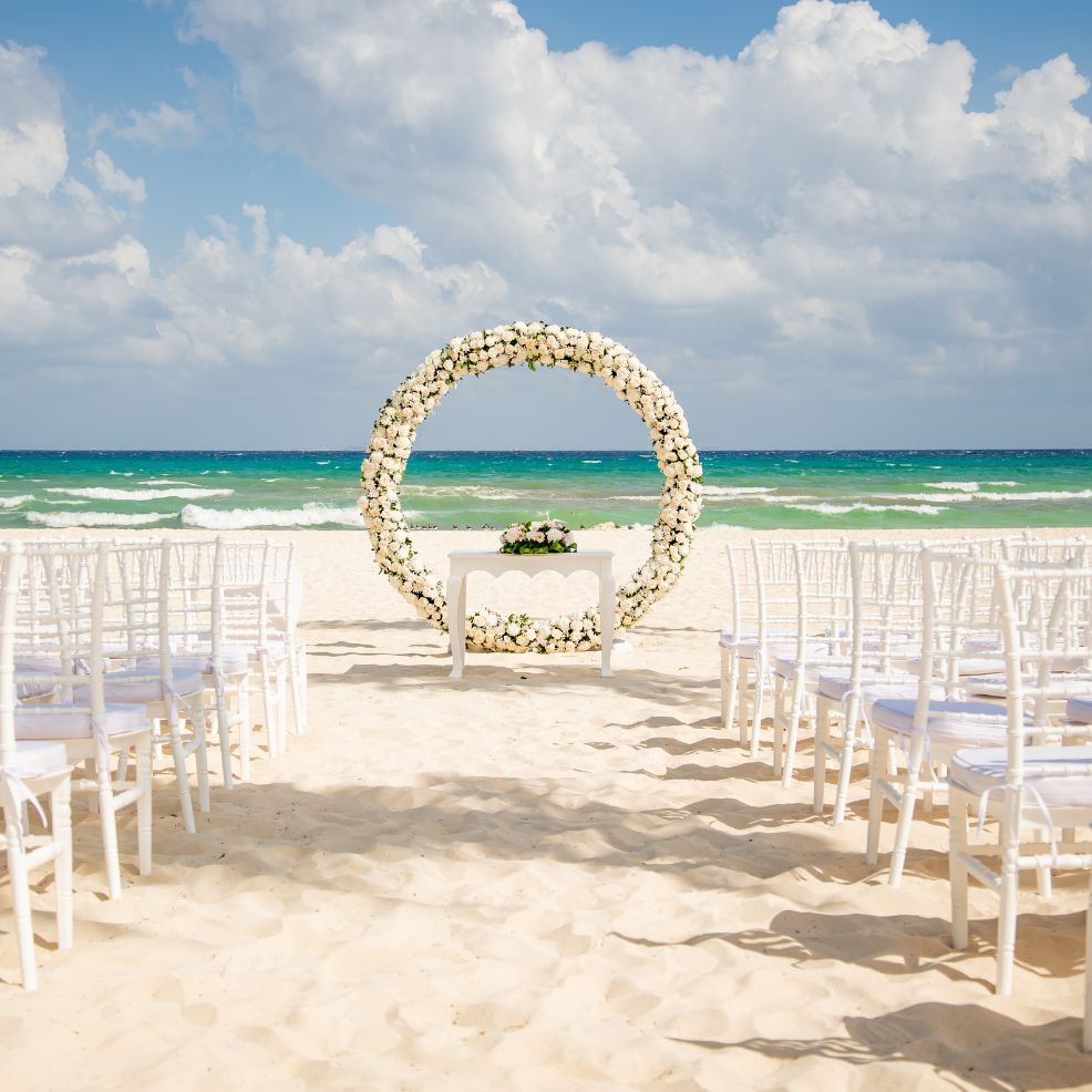 White chairs and a floral arch arranged for a destination wedding ceremony overlooking the ocean.