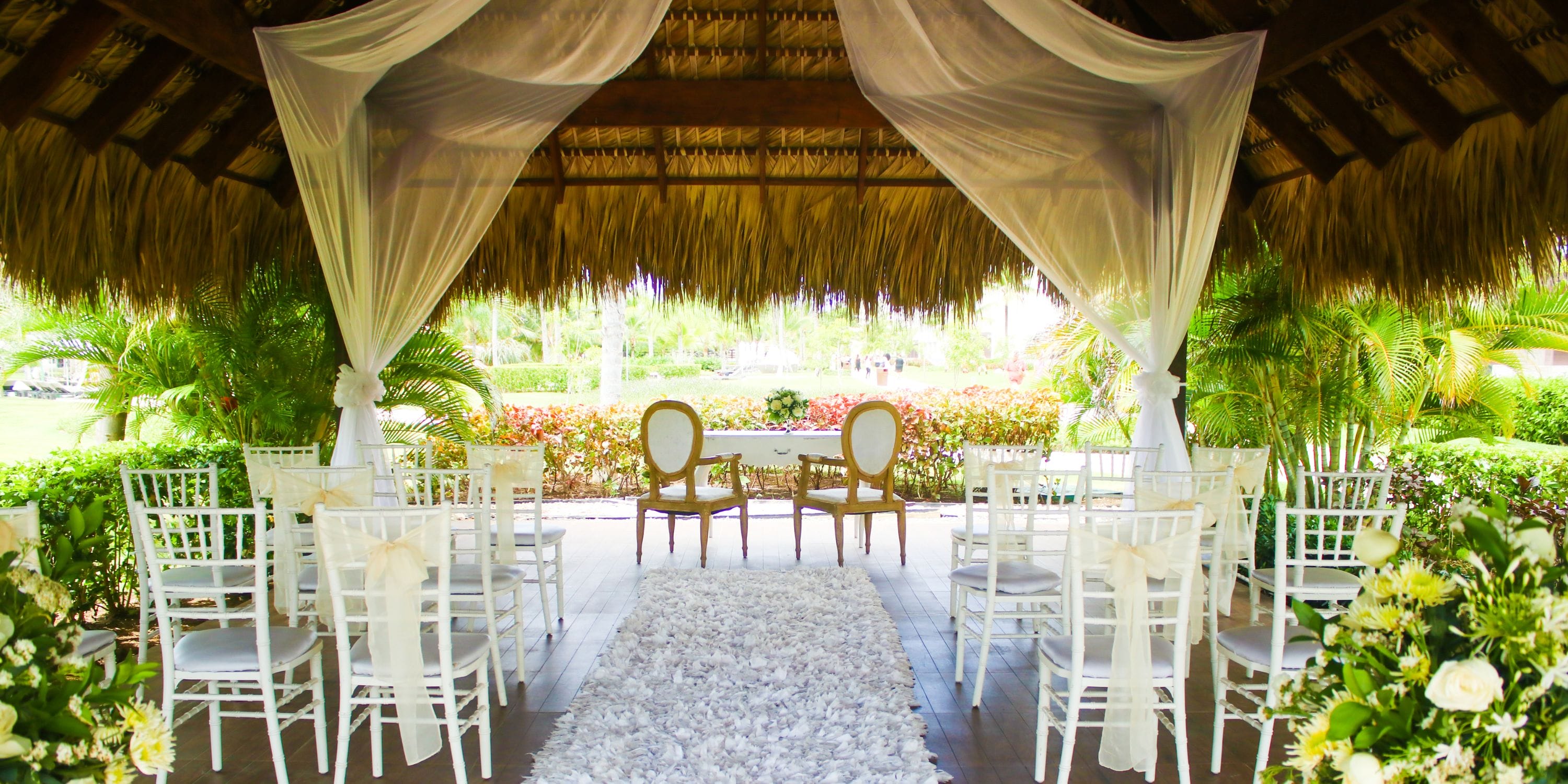 Destination wedding setup at Royalton Bavaro: white chairs, floral d&eacute;cor, and a canopy under a thatched roof.