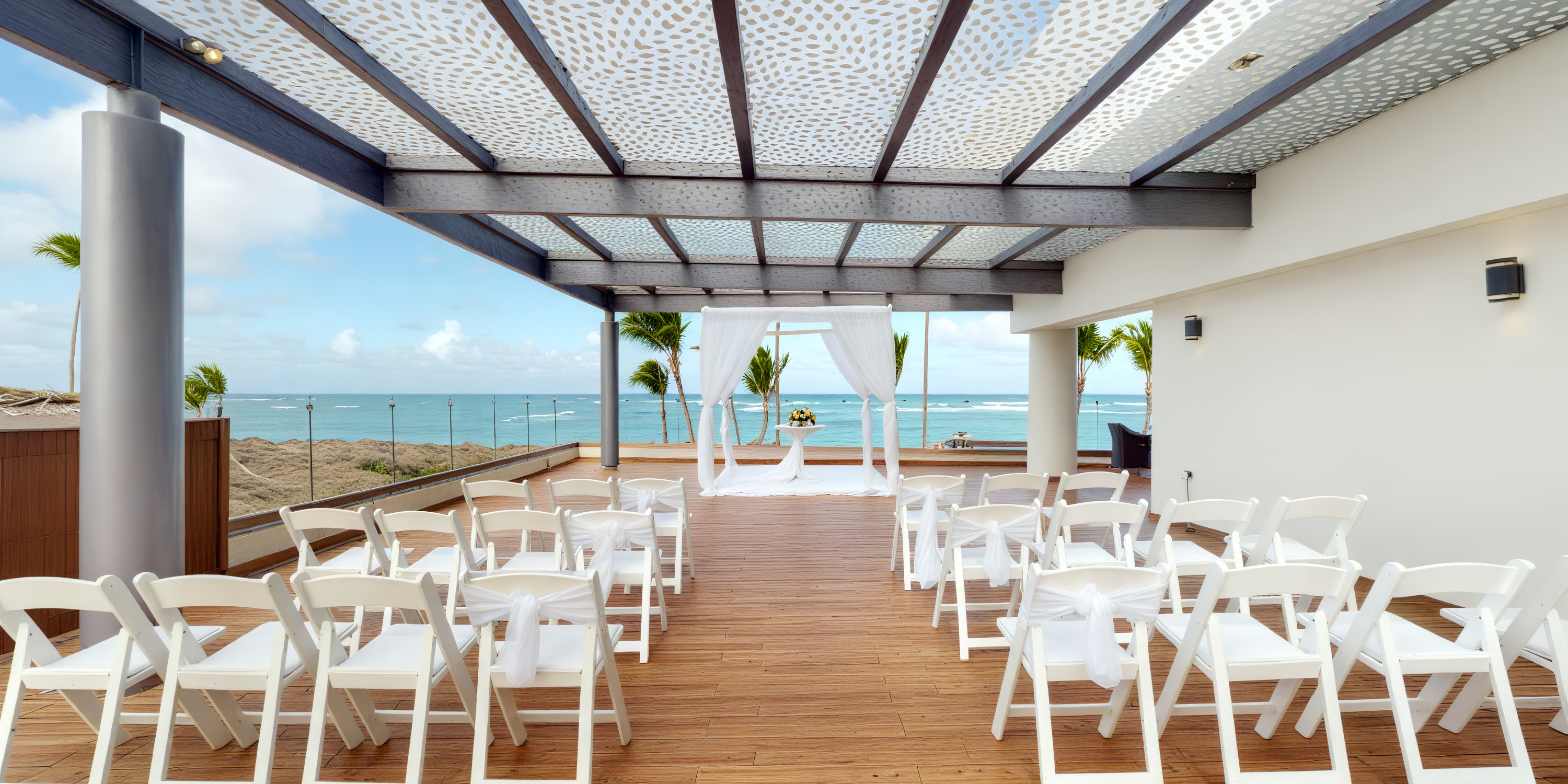 Royalton Bavaro destination wedding setup with white chairs and altar beneath a stylish pergola by the sea.