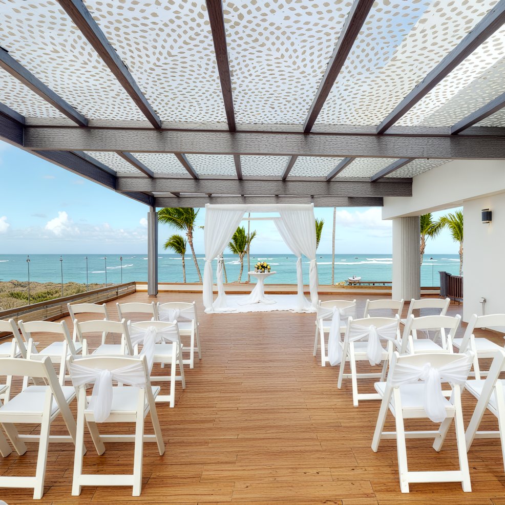 Destination wedding ceremony setup with white chairs and a canopy, set against a scenic ocean backdrop.