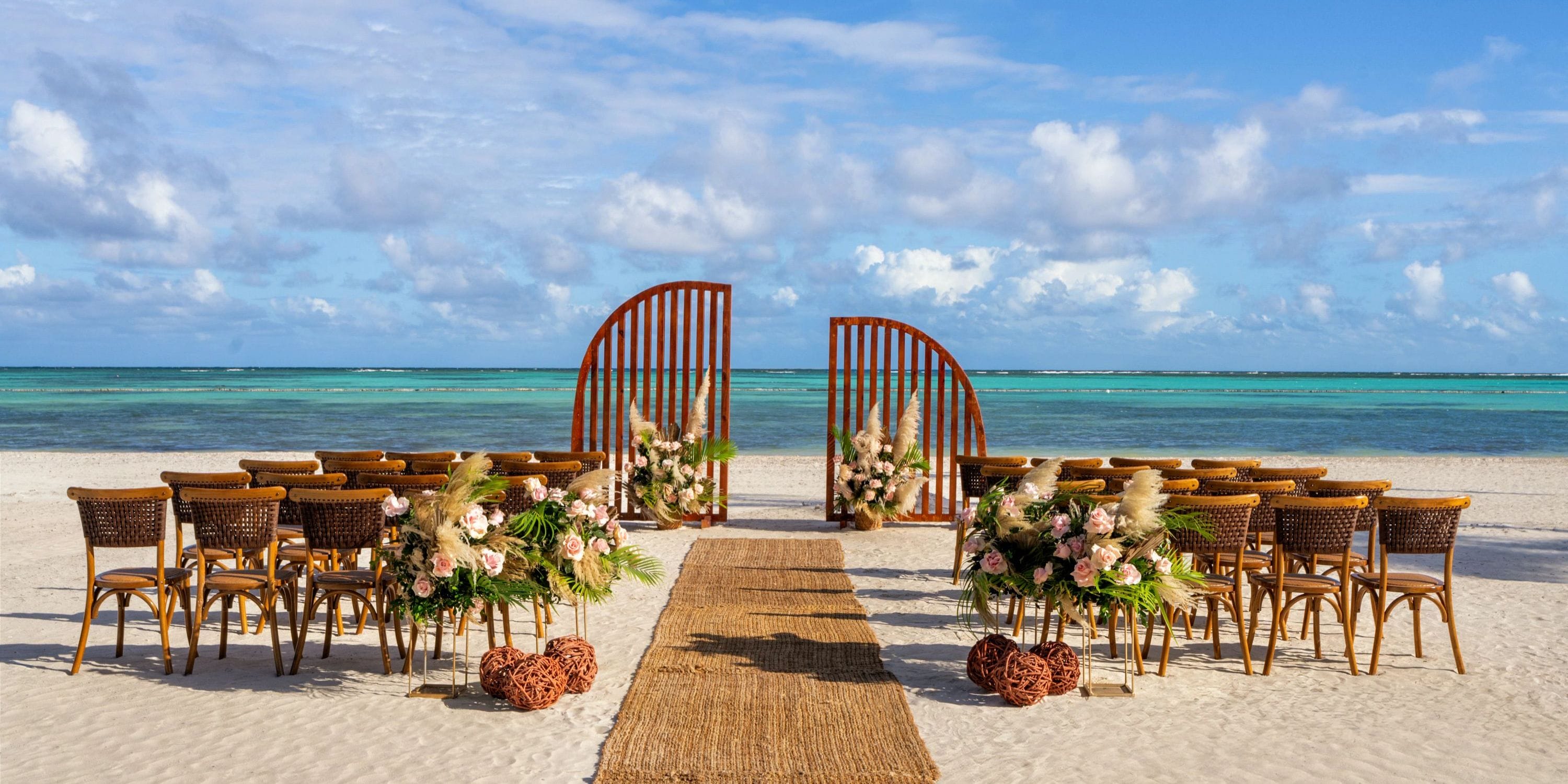 Destination wedding at Secrets Cap Cana featuring oceanfront chairs, floral d&eacute;cor, and a wooden arch.