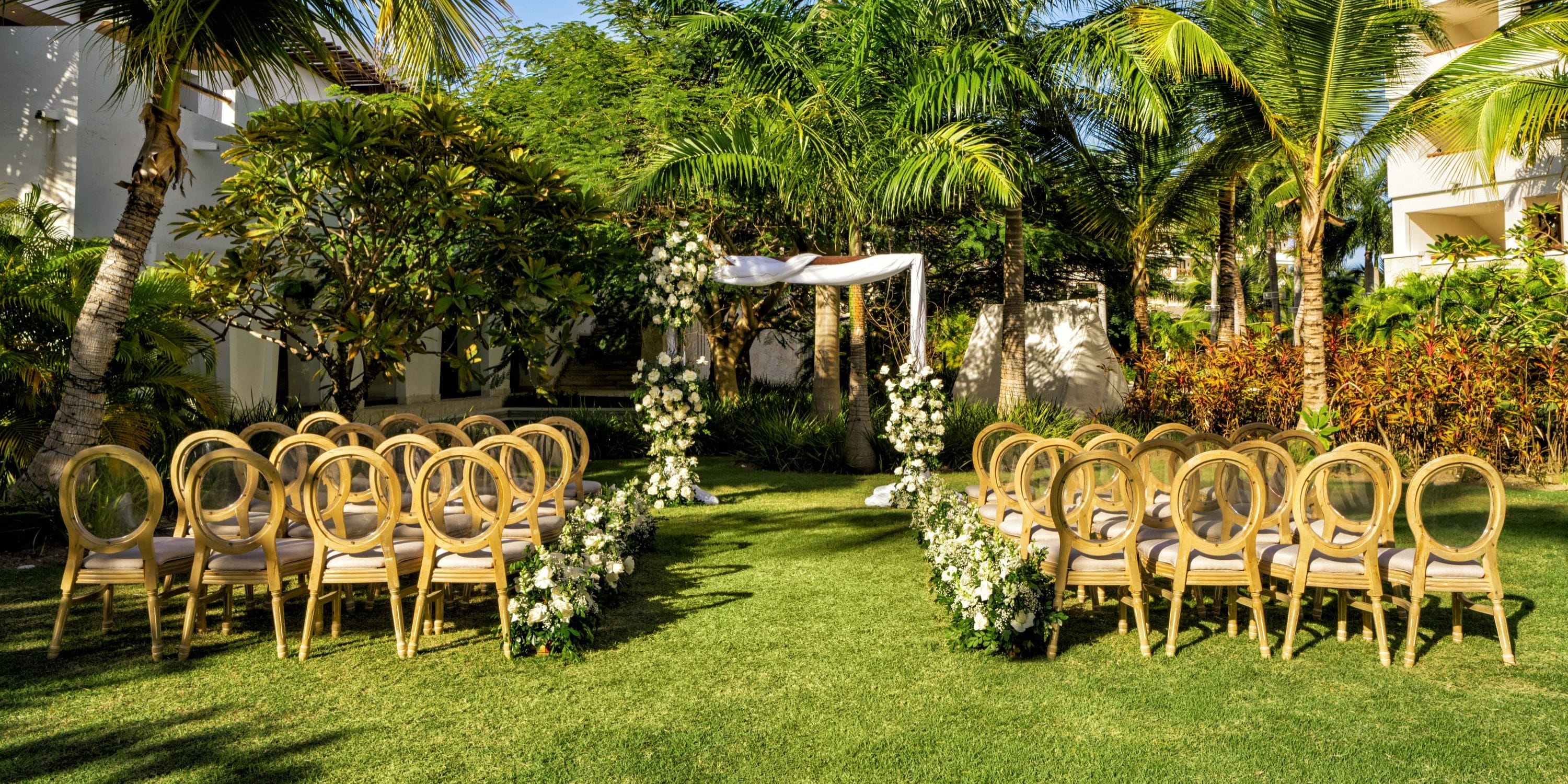 Destination wedding setup at Secrets Cap Cana featuring gold chairs and vibrant florals under palm trees.