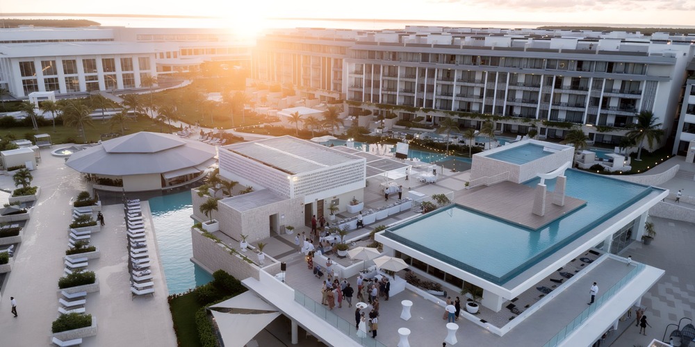 A breathtaking aerial view captures the Majestic Elegance Costa Mujeres resort, showcasing its stunning pools bathed in the warm hues of sunset—a perfect setting for an unforgettable destination wedding.