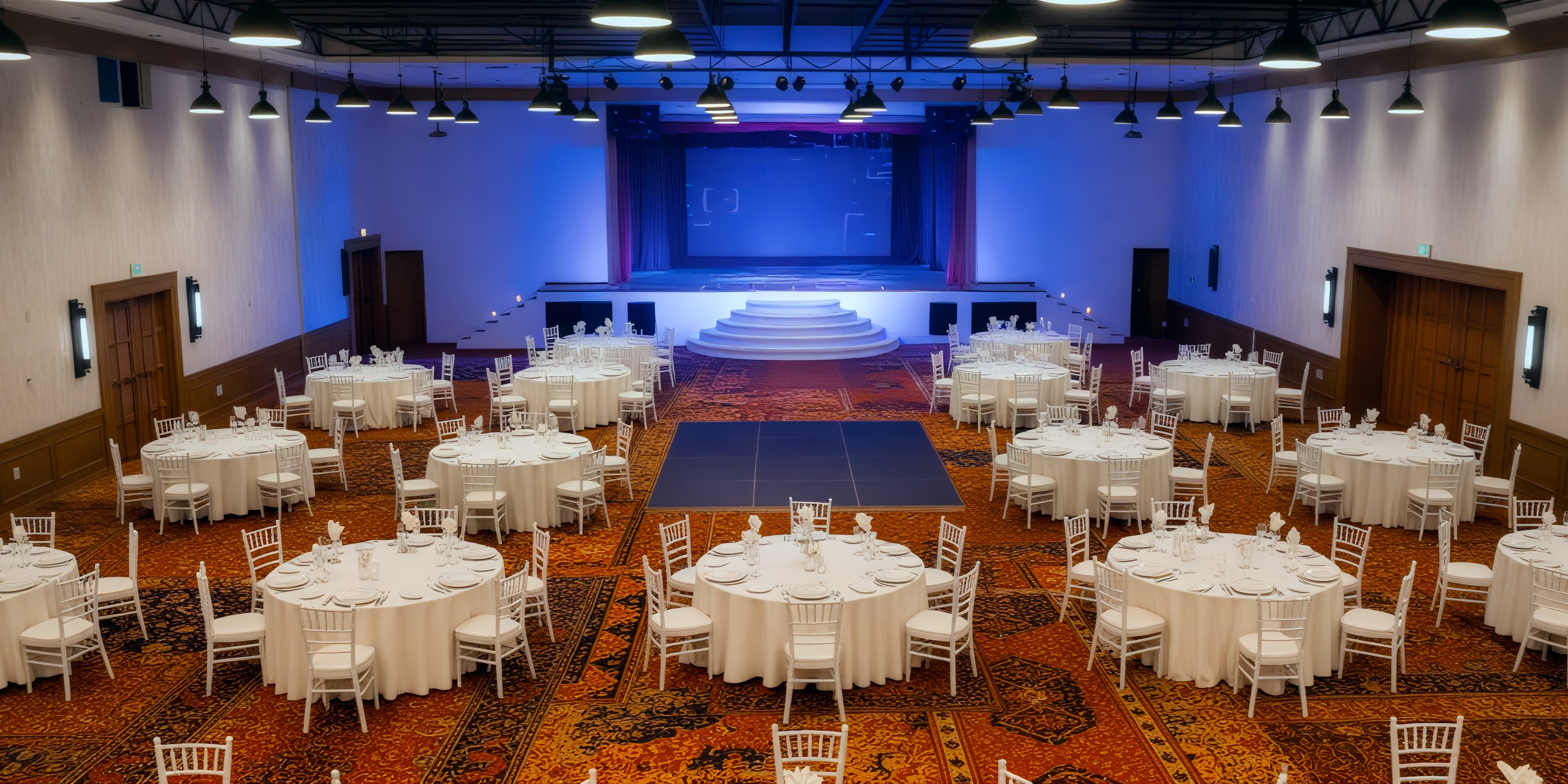 Ballroom at Sunscape Cancun Resort & Spa set for destination wedding, round tables facing blue-lit stage.