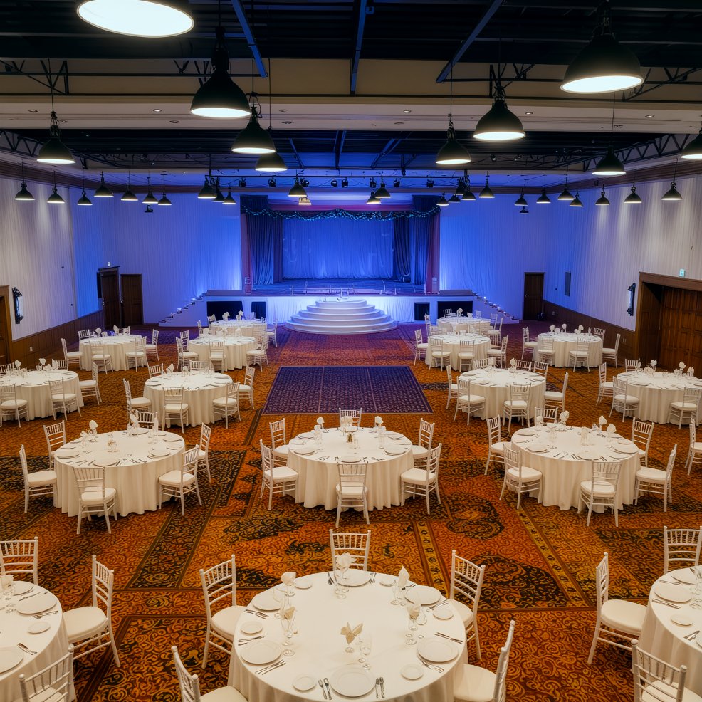 Ballroom set for a destination wedding, round tables arranged toward a blue-lit stage.