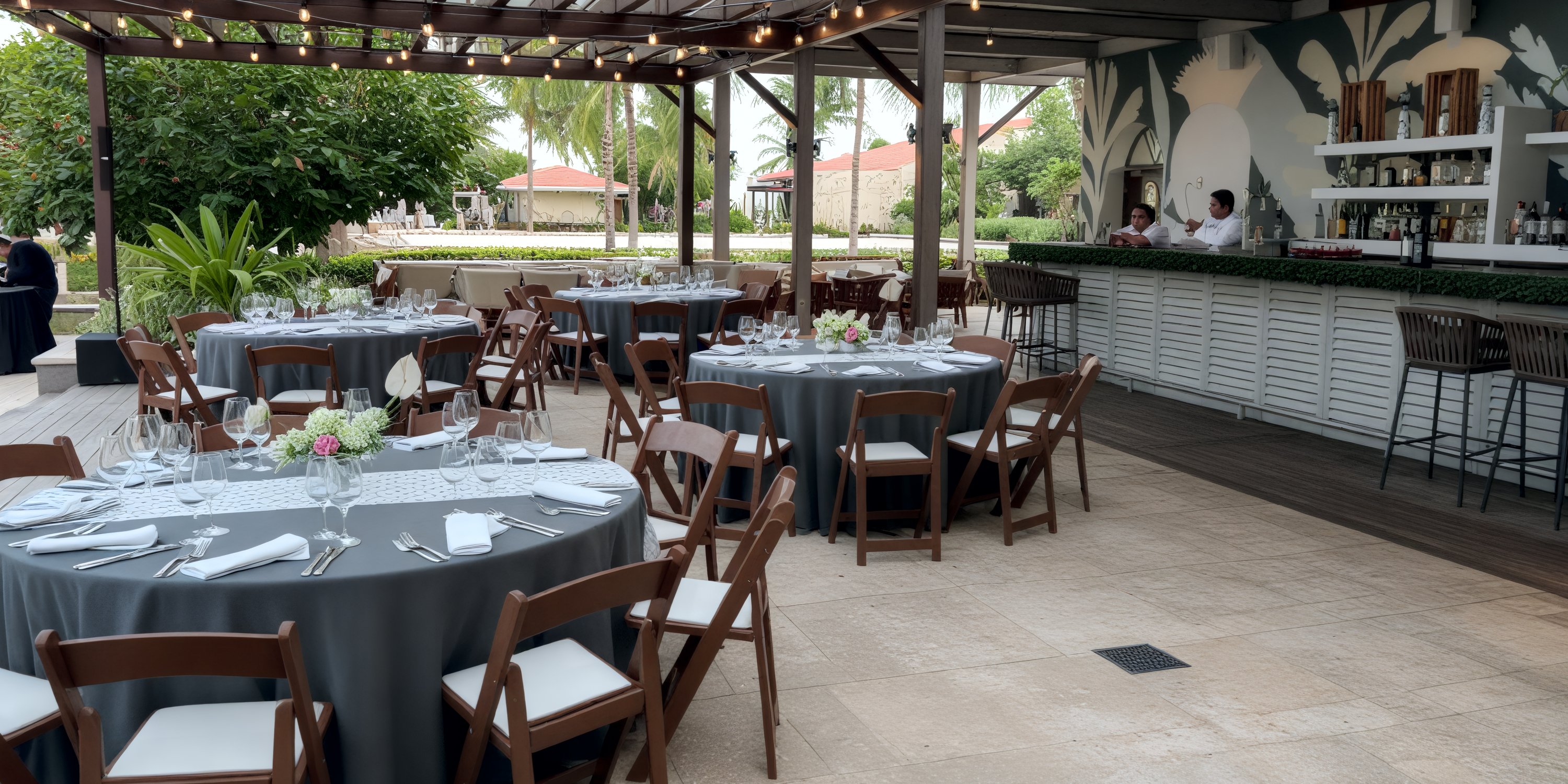 UNICO 20°87° Riviera Maya patio, set for a destination wedding, with round tables and staff near the bar.