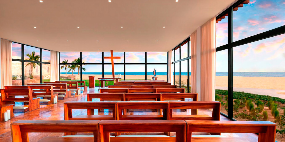 The contemporary interior of Hard Rock Los Cabos features wooden benches oriented towards a substantial cross and altar, with floor-to-ceiling windows providing breathtaking views of the ocean and sky.