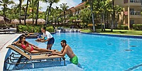 Beautiful couple lounges poolside being waited on by a waitress attendant at the Dreams Punta Cana pool