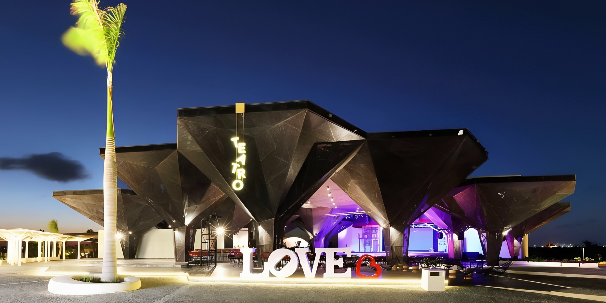 Modern building at twilight with illuminated Grand Palladium Costa Mujeres out front.