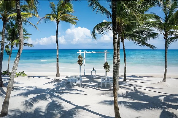 Destination wedding setup at Grand Palladium White Sand: white chairs, arch, palm trees, ocean view.