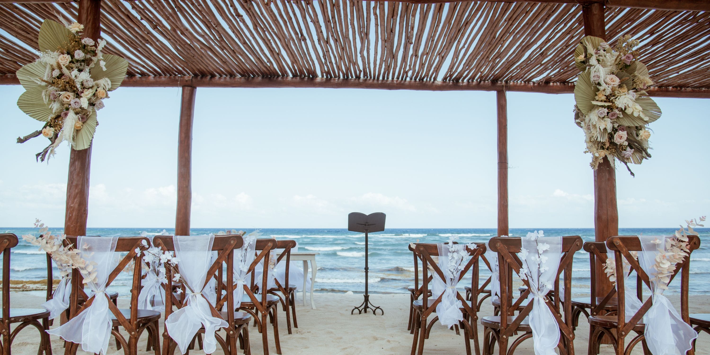 At Bahia Principe Explore Coba, a destination wedding setup with white chairs faces the ocean on the beach.