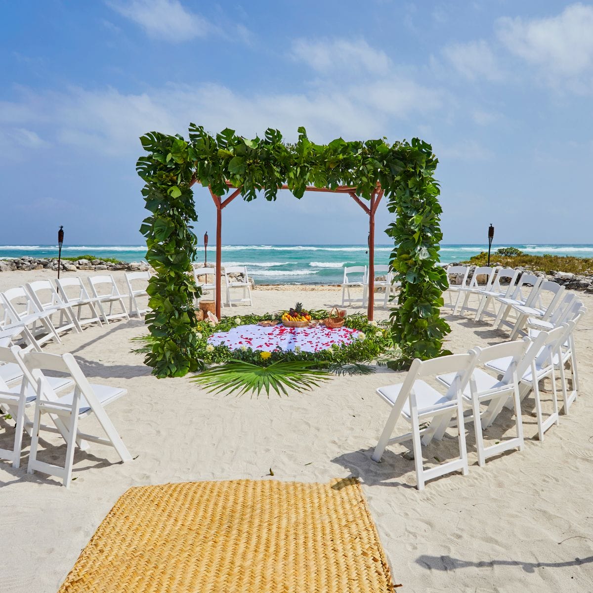 A destination wedding setup with white chairs and a green arch arranged by the ocean.