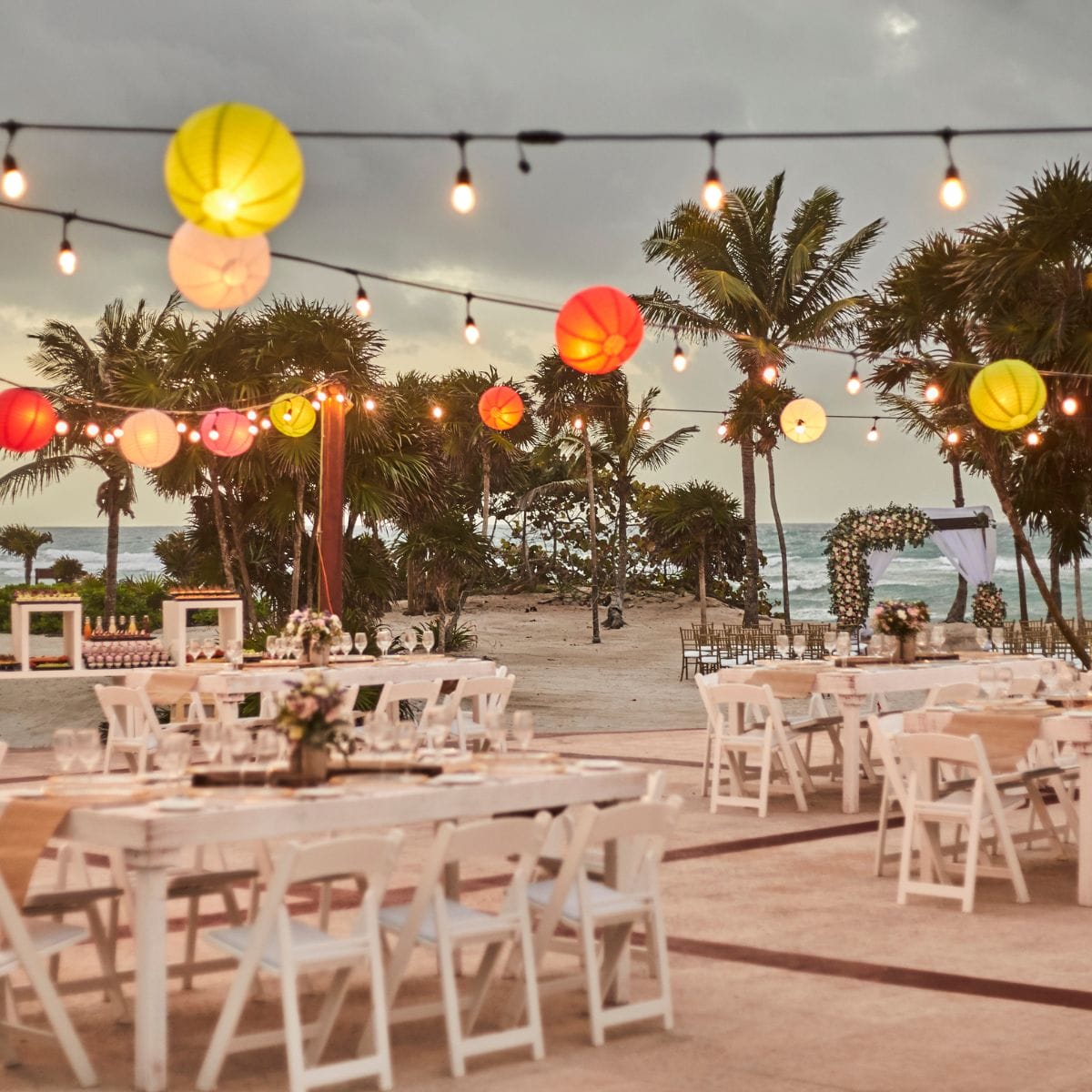 Destination wedding on the beach featuring string lights, paper lanterns, and elegantly decorated tables.