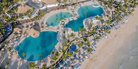A breathtaking aerial view captures the scenic beauty of Grand Punta Cana, featuring its shimmering pools, swaying palm trees, and pristine beach umbrellas along the ocean—a perfect backdrop for a destination wedding.