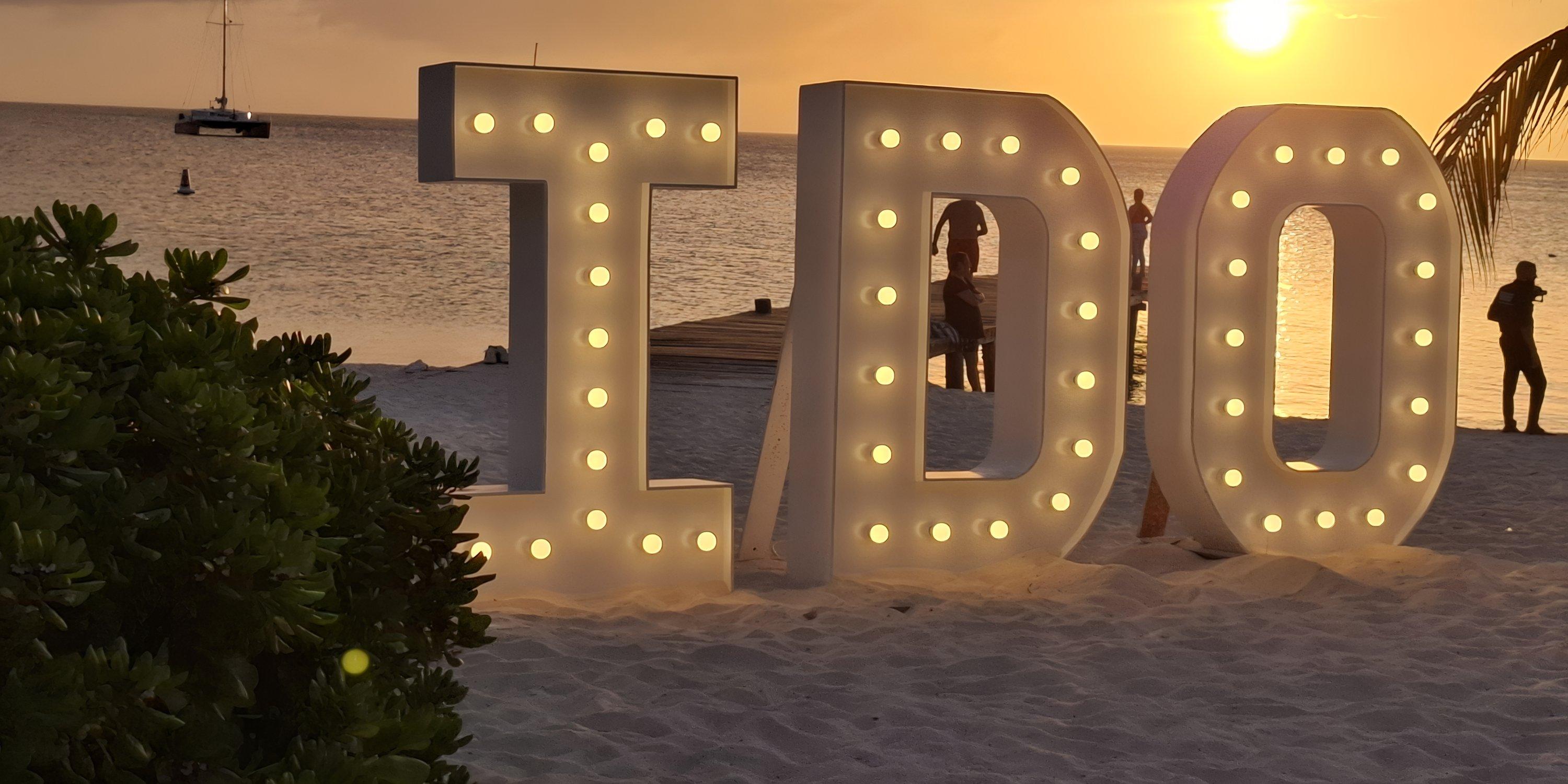 Barcelo Aruba: Illuminated "I DO" letters on a sunset beach, perfect for a destination wedding backdrop.