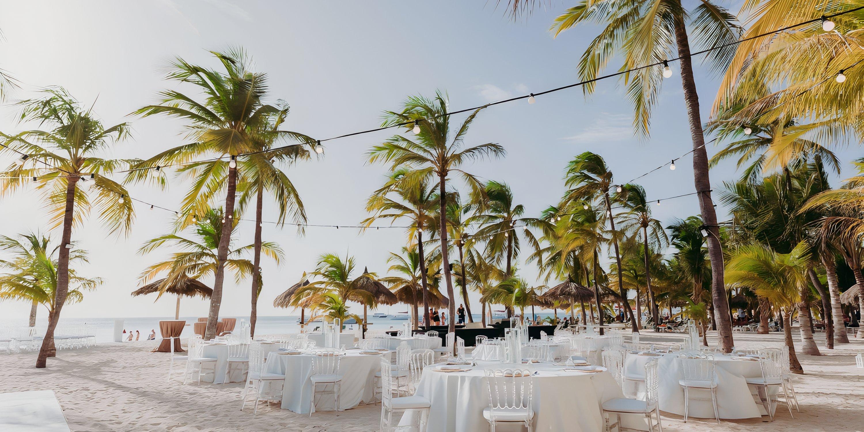 Barcelo Aruba destination wedding setup with round tables, white chairs, palms, and string lights.
