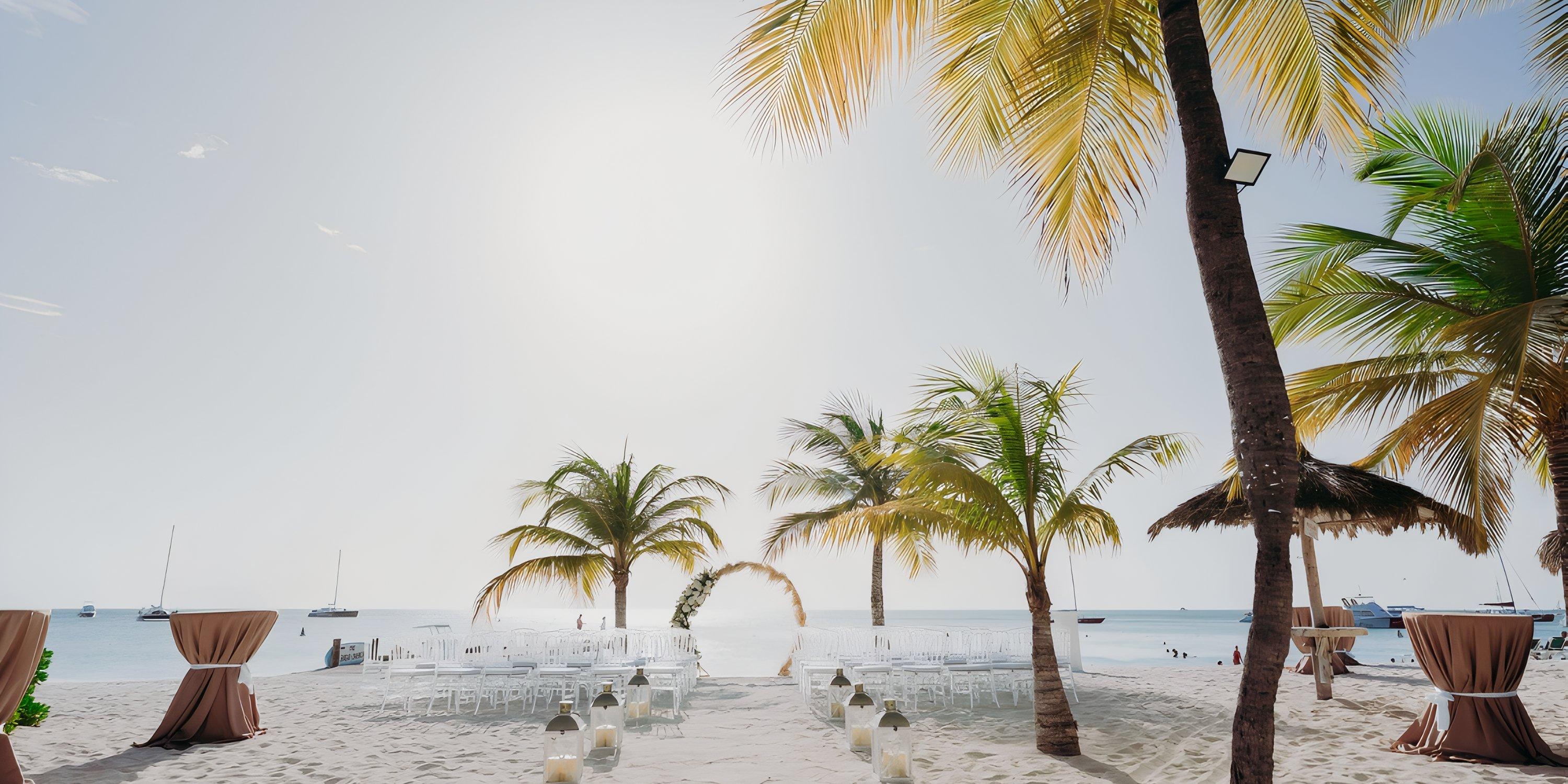 Destination wedding setup at Barcelo Aruba with chairs, tables, and palm trees by the ocean.