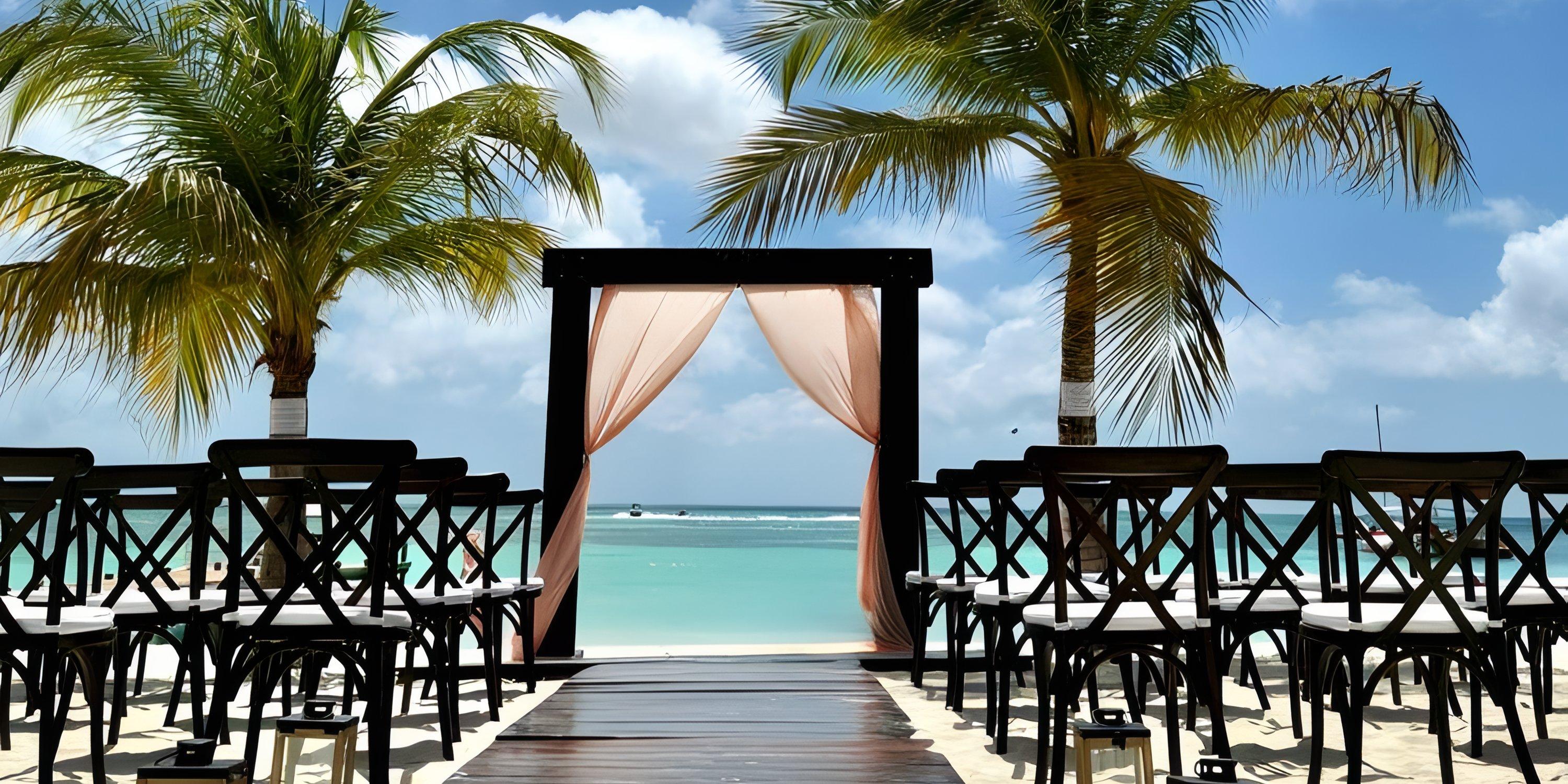 Chairs arranged for a destination wedding face a decorated arch on the sandy beach at Barcelo Aruba.