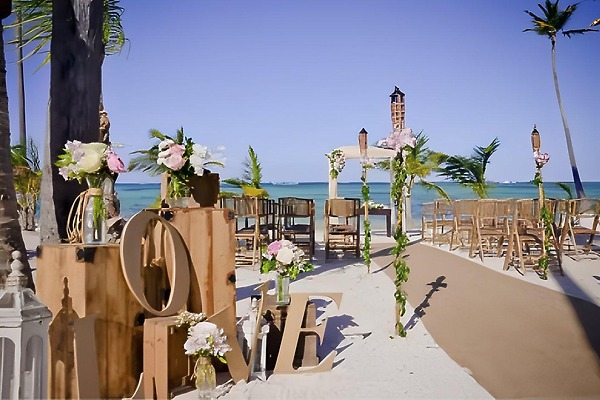 Destination wedding setup at Barcelo Bavaro Beach with wooden chairs, flowers, and "LOVE" letters on sand.