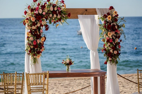Wedding arch with flowers and drapes set up for a destination wedding on the beach facing the ocean.