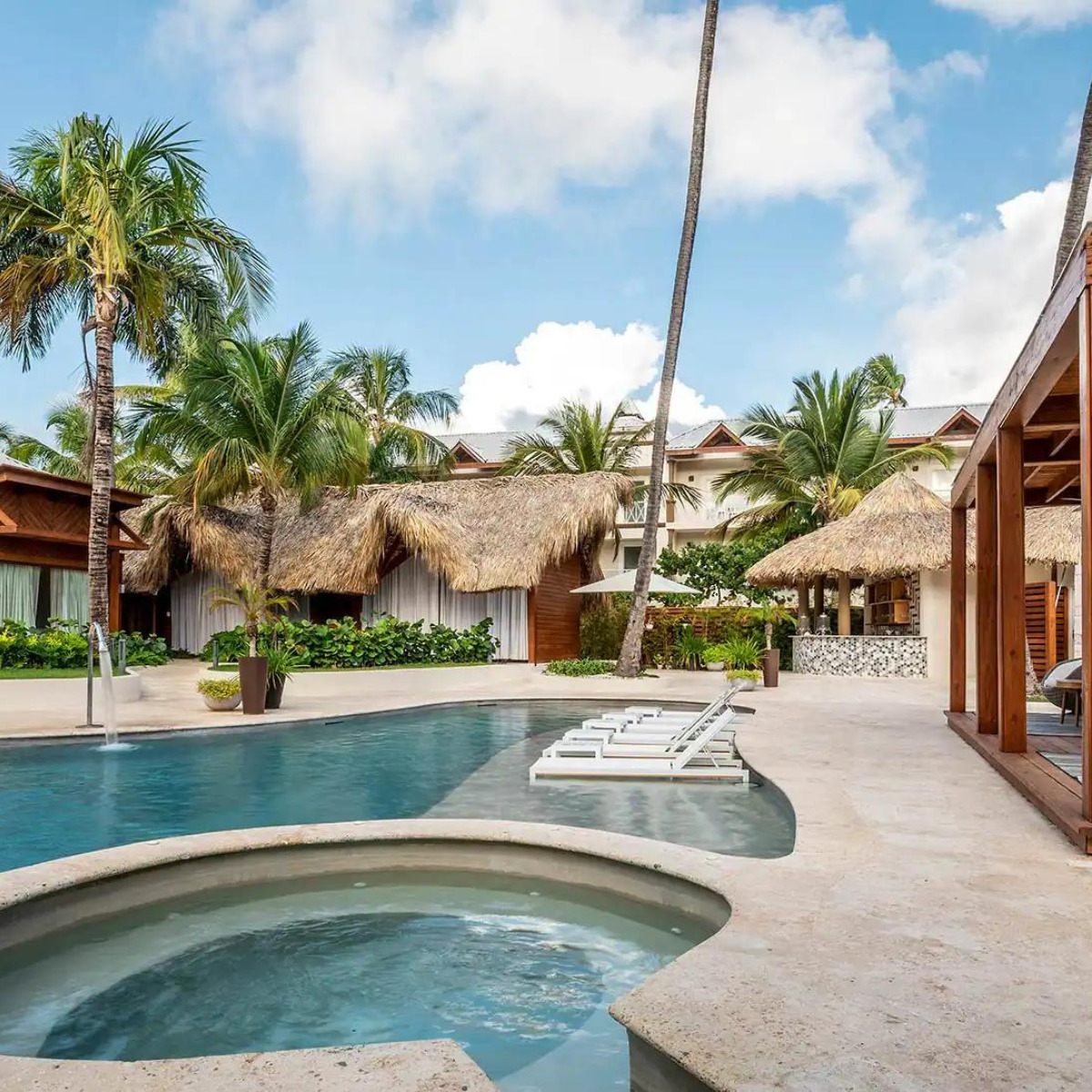 Be Live Collection Punta Cana resort with a swimming pool, hot tub, and palm trees, featuring thatched roof bungalows and sun loungers, perfect for destination weddings.