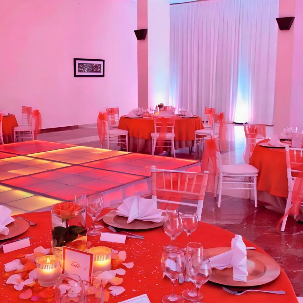 Event hall decorated for destination weddings with red tablecloths, white chairs, and a vibrant light-up dance floor.